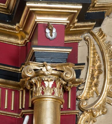 Zdjęcie nr 63: Nastawa architektoniczna, jednoosiowa, jednokondygnacyjna ze zwieńczeniem, ustawiona na dwustrefowym cokole z wyodrębnionymi prostopadłościanami. Ołtarz drewniany, prostopadłościenny z drewnianą mensą. Antepedium wydzielone ramą i wysunięte do przodu, ujęte pilastrami dźwigającymi niepełne belkowanie, w polu wieniec laurowy z rozetą, nad nim kokarda z karbowanej wstęgi flankowana przez dwa podwieszone festony z tkaniny, poniżej wić roślinna. Na ołtarzu ustawione tabernakulum w formie metalowej skrzynki w drewnianej obudowie, ujęte ustawionymi pod kątem spływami wolutowymi. Ścianka frontowa wypukła, z drewnianymi drzwiczkami w kształcie stojącego prostokąta zamkniętego łukiem półkolistym z płaskorzeźbionym kielichem z hostią i kłosami zbóż. Na nim wysoki tron wystawienia z wypukłym frontem z zamontowanym wtórnie nowym tabernakulum (wcześniej obrotowa nisza). Tron ujęty pilastrami ustawionymi pod kątem, o trzonach przechodzących w spływy wolutowe, dekorowane zwisami kwiatowymi; zwieńczony jest trzema rocaille&#039;owymi kabłąkami dekorowanymi zwisami kwiatowymi, podtrzymującymi figurkę pelikana karmiącego młode w gnieździe. Tabernakulum i tron flankowane spływami z podwieszonymi zwisami kwiatowymi zakończonymi cokołami, dźwigającymi przerwany wolutowy przyczółek z figurkami adorujących aniołów; spływy w górnej części zamknięte fragmentami gzymsu z palmetami. 
Nastawa ujęta dwiema parami pilastrów oraz stojącą na ich tle parą kolumn na cokołach dźwigających pełne belkowanie przerwane nad polem środkowym oraz fragmenty przerwanego, wolutowego przyczółka. Przed wewnętrzną parą pilastrów ustawione figury św. Piotra i św. Pawła; na belkowaniu wazony, na przyczółku putta trzymające słońce i księżyc. W polu środkowym podwójna wnęka w formie stojącego prostokąta zamkniętego łukiem odcinkowym nadwieszonym, ujęta profilowaną ramą, ze znacznie mniejszym obrazem Matki Boskiej w kształcie stojącego prostokąta. Nad nią medalion utworzony z wolut i zwisów, zwieńczony koroną otwartą. Zwieńczenie nastawy w formie trapezu ujętego wolutami spływającymi na belkowanie, zamknięte fragmentem falistego gzymsu, dekorowanym medalionem z Okiem Opatrzności w otoku z obłoków w glorii promienistej oraz gałązkami kwiatowymi. W polu obraz św. Katarzyny w formie zbliżonej do zwieńczenia, o ściętych dolnych narożach, w profilowanej ramie, z gałązkami kwiatowymi. 
Nastawa flankowana uszami utworzonymi z rocaille&#039;u, przytwierdzonymi do ściany. Ujęta parą wsporników na trumienki relikwiarzowe oraz parą dużych konsol dekorowanych rocaille&#039;m z figurami św. Mikołaja i św. Stanisława. Struktura polichromowana w kolorze głębokiej czerwieni z czarnymi profilami; kolumny, ornamentyka i profile złocone i srebrzone.