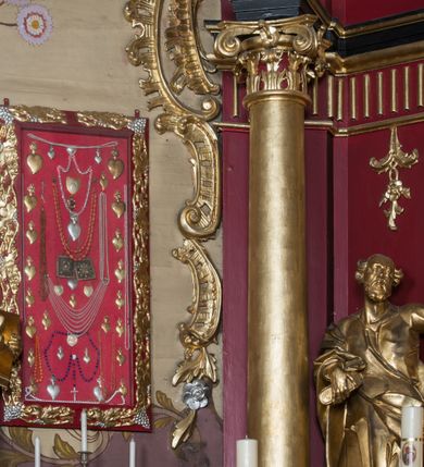 Zdjęcie nr 65: Nastawa architektoniczna, jednoosiowa, jednokondygnacyjna ze zwieńczeniem, ustawiona na dwustrefowym cokole z wyodrębnionymi prostopadłościanami. Ołtarz drewniany, prostopadłościenny z drewnianą mensą. Antepedium wydzielone ramą i wysunięte do przodu, ujęte pilastrami dźwigającymi niepełne belkowanie, w polu wieniec laurowy z rozetą, nad nim kokarda z karbowanej wstęgi flankowana przez dwa podwieszone festony z tkaniny, poniżej wić roślinna. Na ołtarzu ustawione tabernakulum w formie metalowej skrzynki w drewnianej obudowie, ujęte ustawionymi pod kątem spływami wolutowymi. Ścianka frontowa wypukła, z drewnianymi drzwiczkami w kształcie stojącego prostokąta zamkniętego łukiem półkolistym z płaskorzeźbionym kielichem z hostią i kłosami zbóż. Na nim wysoki tron wystawienia z wypukłym frontem z zamontowanym wtórnie nowym tabernakulum (wcześniej obrotowa nisza). Tron ujęty pilastrami ustawionymi pod kątem, o trzonach przechodzących w spływy wolutowe, dekorowane zwisami kwiatowymi; zwieńczony jest trzema rocaille&#039;owymi kabłąkami dekorowanymi zwisami kwiatowymi, podtrzymującymi figurkę pelikana karmiącego młode w gnieździe. Tabernakulum i tron flankowane spływami z podwieszonymi zwisami kwiatowymi zakończonymi cokołami, dźwigającymi przerwany wolutowy przyczółek z figurkami adorujących aniołów; spływy w górnej części zamknięte fragmentami gzymsu z palmetami. 
Nastawa ujęta dwiema parami pilastrów oraz stojącą na ich tle parą kolumn na cokołach dźwigających pełne belkowanie przerwane nad polem środkowym oraz fragmenty przerwanego, wolutowego przyczółka. Przed wewnętrzną parą pilastrów ustawione figury św. Piotra i św. Pawła; na belkowaniu wazony, na przyczółku putta trzymające słońce i księżyc. W polu środkowym podwójna wnęka w formie stojącego prostokąta zamkniętego łukiem odcinkowym nadwieszonym, ujęta profilowaną ramą, ze znacznie mniejszym obrazem Matki Boskiej w kształcie stojącego prostokąta. Nad nią medalion utworzony z wolut i zwisów, zwieńczony koroną otwartą. Zwieńczenie nastawy w formie trapezu ujętego wolutami spływającymi na belkowanie, zamknięte fragmentem falistego gzymsu, dekorowanym medalionem z Okiem Opatrzności w otoku z obłoków w glorii promienistej oraz gałązkami kwiatowymi. W polu obraz św. Katarzyny w formie zbliżonej do zwieńczenia, o ściętych dolnych narożach, w profilowanej ramie, z gałązkami kwiatowymi. 
Nastawa flankowana uszami utworzonymi z rocaille&#039;u, przytwierdzonymi do ściany. Ujęta parą wsporników na trumienki relikwiarzowe oraz parą dużych konsol dekorowanych rocaille&#039;m z figurami św. Mikołaja i św. Stanisława. Struktura polichromowana w kolorze głębokiej czerwieni z czarnymi profilami; kolumny, ornamentyka i profile złocone i srebrzone.