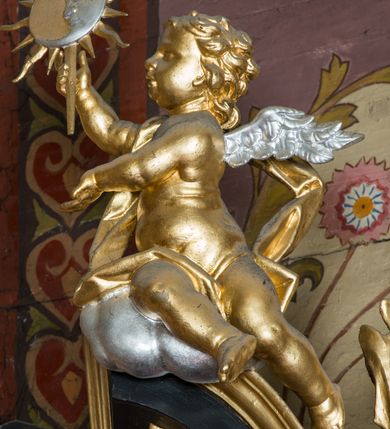 Zdjęcie nr 85: Nastawa architektoniczna, jednoosiowa, jednokondygnacyjna ze zwieńczeniem, ustawiona na dwustrefowym cokole z wyodrębnionymi prostopadłościanami. Ołtarz drewniany, prostopadłościenny z drewnianą mensą. Antepedium wydzielone ramą i wysunięte do przodu, ujęte pilastrami dźwigającymi niepełne belkowanie, w polu wieniec laurowy z rozetą, nad nim kokarda z karbowanej wstęgi flankowana przez dwa podwieszone festony z tkaniny, poniżej wić roślinna. Na ołtarzu ustawione tabernakulum w formie metalowej skrzynki w drewnianej obudowie, ujęte ustawionymi pod kątem spływami wolutowymi. Ścianka frontowa wypukła, z drewnianymi drzwiczkami w kształcie stojącego prostokąta zamkniętego łukiem półkolistym z płaskorzeźbionym kielichem z hostią i kłosami zbóż. Na nim wysoki tron wystawienia z wypukłym frontem z zamontowanym wtórnie nowym tabernakulum (wcześniej obrotowa nisza). Tron ujęty pilastrami ustawionymi pod kątem, o trzonach przechodzących w spływy wolutowe, dekorowane zwisami kwiatowymi; zwieńczony jest trzema rocaille&#039;owymi kabłąkami dekorowanymi zwisami kwiatowymi, podtrzymującymi figurkę pelikana karmiącego młode w gnieździe. Tabernakulum i tron flankowane spływami z podwieszonymi zwisami kwiatowymi zakończonymi cokołami, dźwigającymi przerwany wolutowy przyczółek z figurkami adorujących aniołów; spływy w górnej części zamknięte fragmentami gzymsu z palmetami. 
Nastawa ujęta dwiema parami pilastrów oraz stojącą na ich tle parą kolumn na cokołach dźwigających pełne belkowanie przerwane nad polem środkowym oraz fragmenty przerwanego, wolutowego przyczółka. Przed wewnętrzną parą pilastrów ustawione figury św. Piotra i św. Pawła; na belkowaniu wazony, na przyczółku putta trzymające słońce i księżyc. W polu środkowym podwójna wnęka w formie stojącego prostokąta zamkniętego łukiem odcinkowym nadwieszonym, ujęta profilowaną ramą, ze znacznie mniejszym obrazem Matki Boskiej w kształcie stojącego prostokąta. Nad nią medalion utworzony z wolut i zwisów, zwieńczony koroną otwartą. Zwieńczenie nastawy w formie trapezu ujętego wolutami spływającymi na belkowanie, zamknięte fragmentem falistego gzymsu, dekorowanym medalionem z Okiem Opatrzności w otoku z obłoków w glorii promienistej oraz gałązkami kwiatowymi. W polu obraz św. Katarzyny w formie zbliżonej do zwieńczenia, o ściętych dolnych narożach, w profilowanej ramie, z gałązkami kwiatowymi. 
Nastawa flankowana uszami utworzonymi z rocaille&#039;u, przytwierdzonymi do ściany. Ujęta parą wsporników na trumienki relikwiarzowe oraz parą dużych konsol dekorowanych rocaille&#039;m z figurami św. Mikołaja i św. Stanisława. Struktura polichromowana w kolorze głębokiej czerwieni z czarnymi profilami; kolumny, ornamentyka i profile złocone i srebrzone.