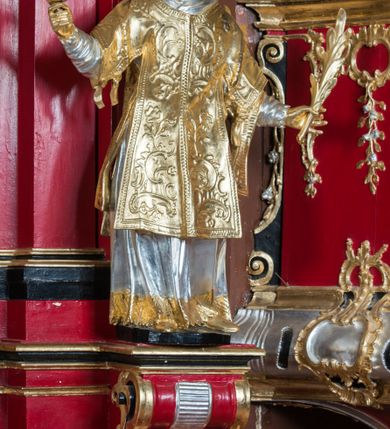 Zdjęcie nr 2: Rzeźba ścięta z tyłu i drążona, ustawiona na niskiej podstawie. Święty ukazany frontalnie, z głową skierowaną w prawo, w kontrapoście, o sylwetce lekko przechylonej w tył. W prawej, uniesionej ręce trzyma kamień, w lewej wysuniętej w bok liść palmy. Twarz ma szczupłą, kwadratową, o wyraźnie zarysowanej żuchwie, niewielkich, migdałowatych oczach, osadzonych blisko siebie, małym nosie i wąskich ustach. Włosy krótkie, silnie kręcone. Święty ubrany jest w albę, stułę skrzyżowaną na prawym boku, humerał, dalmatykę z płaskorzeźbionym wzorem kwiatowym i rocaille'em, na lewym przedramieniu ma manipularz. Figura niemal w całości złocona, alba i humerał srebrzone.