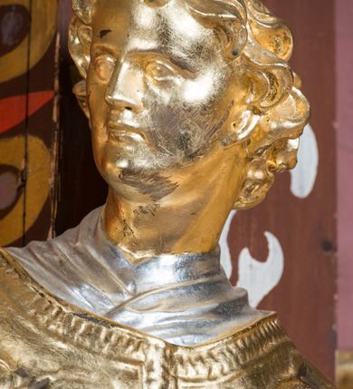 Zdjęcie nr 10: Rzeźba ścięta z tyłu i drążona, ustawiona na niskiej podstawie. Święty ukazany frontalnie, z głową skierowaną w prawo, w kontrapoście, o sylwetce lekko przechylonej w tył. W prawej, uniesionej ręce trzyma kamień, w lewej wysuniętej w bok liść palmy. Twarz ma szczupłą, kwadratową, o wyraźnie zarysowanej żuchwie, niewielkich, migdałowatych oczach, osadzonych blisko siebie, małym nosie i wąskich ustach. Włosy krótkie, silnie kręcone. Święty ubrany jest w albę, stułę skrzyżowaną na prawym boku, humerał, dalmatykę z płaskorzeźbionym wzorem kwiatowym i rocaille&#039;em, na lewym przedramieniu ma manipularz. Figura niemal w całości złocona, alba i humerał srebrzone.