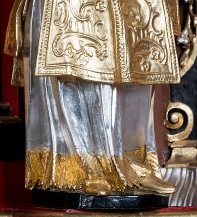 Zdjęcie nr 7: Rzeźba ścięta z tyłu i drążona, ustawiona na niskiej podstawie. Święty ukazany frontalnie, z głową skierowaną w prawo, w kontrapoście, o sylwetce lekko przechylonej w tył. W prawej, uniesionej ręce trzyma kamień, w lewej wysuniętej w bok liść palmy. Twarz ma szczupłą, kwadratową, o wyraźnie zarysowanej żuchwie, niewielkich, migdałowatych oczach, osadzonych blisko siebie, małym nosie i wąskich ustach. Włosy krótkie, silnie kręcone. Święty ubrany jest w albę, stułę skrzyżowaną na prawym boku, humerał, dalmatykę z płaskorzeźbionym wzorem kwiatowym i rocaille'em, na lewym przedramieniu ma manipularz. Figura niemal w całości złocona, alba i humerał srebrzone.