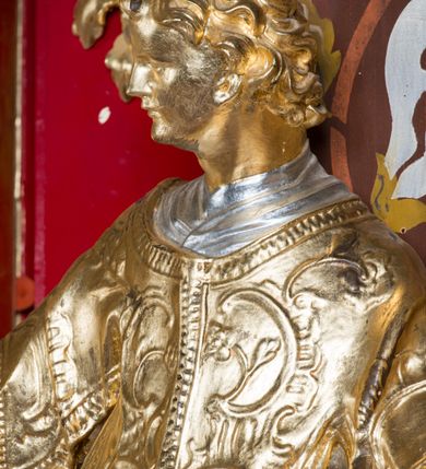 Zdjęcie nr 13: Rzeźba ścięta z tyłu i drążona, ustawiona na niskiej podstawie. Święty ukazany frontalnie, z głową skierowaną w prawo, w kontrapoście, o sylwetce lekko przechylonej w tył. W prawej, uniesionej ręce trzyma kamień, w lewej wysuniętej w bok liść palmy. Twarz ma szczupłą, kwadratową, o wyraźnie zarysowanej żuchwie, niewielkich, migdałowatych oczach, osadzonych blisko siebie, małym nosie i wąskich ustach. Włosy krótkie, silnie kręcone. Święty ubrany jest w albę, stułę skrzyżowaną na prawym boku, humerał, dalmatykę z płaskorzeźbionym wzorem kwiatowym i rocaille'em, na lewym przedramieniu ma manipularz. Figura niemal w całości złocona, alba i humerał srebrzone.