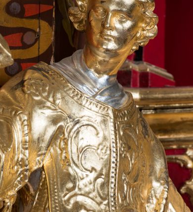 Zdjęcie nr 4: Rzeźba ścięta z tyłu i drążona, ustawiona na niskiej podstawie. Święty ukazany frontalnie, z głową skierowaną w prawo, w kontrapoście, o sylwetce lekko przechylonej w tył. W prawej, uniesionej ręce trzyma kamień, w lewej wysuniętej w bok liść palmy. Twarz ma szczupłą, kwadratową, o wyraźnie zarysowanej żuchwie, niewielkich, migdałowatych oczach, osadzonych blisko siebie, małym nosie i wąskich ustach. Włosy krótkie, silnie kręcone. Święty ubrany jest w albę, stułę skrzyżowaną na prawym boku, humerał, dalmatykę z płaskorzeźbionym wzorem kwiatowym i rocaille'em, na lewym przedramieniu ma manipularz. Figura niemal w całości złocona, alba i humerał srebrzone.