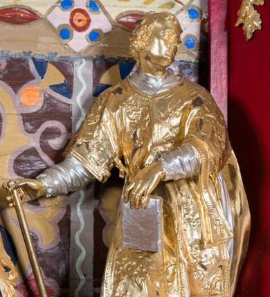 Zdjęcie nr 1: Rzeźba drążona, ustawiona na niskiej podstawie. Święty zwrócony w trzech czwartych w prawo, z uniesioną głową skierowaną w lewo, w kontrapoście, o esowato wygiętej sylwetce. W lewej ręce trzyma księgę opartą na prawym udzie, w prawej, wyciągniętej w bok trzyma ruszt. Twarz ma szczupłą, kwadratową, z wyraźnie zarysowaną żuchwą, niewielkimi, migdałowatymi oczami, osadzonymi blisko siebie, małym nosem i wąskimi ustami. Włosy krótkie, silnie kręcone. Święty ubrany jest w albę przewiązaną w talii, dalmatykę dekorowaną płaskorzeźbionym wzorem roślinnym, na lewym przedramieniu ma manipularz. Figura niemal w całości złocona, jedynie alba i księga są srebrzone.