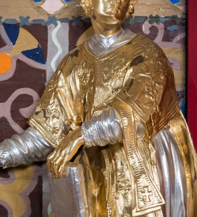 Zdjęcie nr 2: Rzeźba drążona, ustawiona na niskiej podstawie. Święty zwrócony w trzech czwartych w prawo, z uniesioną głową skierowaną w lewo, w kontrapoście, o esowato wygiętej sylwetce. W lewej ręce trzyma księgę opartą na prawym udzie, w prawej, wyciągniętej w bok trzyma ruszt. Twarz ma szczupłą, kwadratową, z wyraźnie zarysowaną żuchwą, niewielkimi, migdałowatymi oczami, osadzonymi blisko siebie, małym nosem i wąskimi ustami. Włosy krótkie, silnie kręcone. Święty ubrany jest w albę przewiązaną w talii, dalmatykę dekorowaną płaskorzeźbionym wzorem roślinnym, na lewym przedramieniu ma manipularz. Figura niemal w całości złocona, jedynie alba i księga są srebrzone.