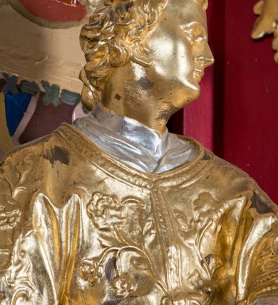 Zdjęcie nr 7: Rzeźba drążona, ustawiona na niskiej podstawie. Święty zwrócony w trzech czwartych w prawo, z uniesioną głową skierowaną w lewo, w kontrapoście, o esowato wygiętej sylwetce. W lewej ręce trzyma księgę opartą na prawym udzie, w prawej, wyciągniętej w bok trzyma ruszt. Twarz ma szczupłą, kwadratową, z wyraźnie zarysowaną żuchwą, niewielkimi, migdałowatymi oczami, osadzonymi blisko siebie, małym nosem i wąskimi ustami. Włosy krótkie, silnie kręcone. Święty ubrany jest w albę przewiązaną w talii, dalmatykę dekorowaną płaskorzeźbionym wzorem roślinnym, na lewym przedramieniu ma manipularz. Figura niemal w całości złocona, jedynie alba i księga są srebrzone.