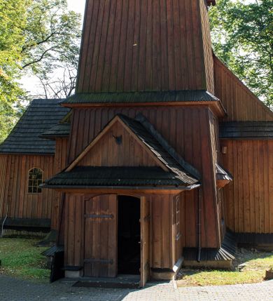 Zdjęcie nr 1: Kościół parafialny w Gruszowie znajduje się na niewielkim wzniesieniu w centrum miejscowości. Budowla jest orientowana, jednonawowa, z szerokim zamkniętym trójbocznie prezbiterium oraz czworoboczną wieżą od zachodu. Korpusu nawowy i prezbiterium charakteryzuje konstrukcja zrębowa, natomiast wieżę słupowa. Od północy do prezbiterium przylega zakrystia na rzucie prostokąta, natomiast do nawy zamknięta trójbocznie kaplica boczna. Do wnętrza kościoła prowadzą dwie kruchty, jedna od strony południowej, druga przez wieżę od zachodniej. Nad korpusem nawowym i prezbiterium znajduje się jednokalenicowy dach kryty gontem, a na styku nawy i prezbiterium usytuowana jest drewniana wieżyczka na sygnaturkę nakryta baniastym hełmem z latarnią. Zakrystia przekryta jest dachem pulpitowym, natomiast kaplica boczna oraz kruchty dachami dwuspadowymi krytymi gontem. Izbicową, o pochyłych ścianach wieżę wieńczy okuty blachą dach namiotowy. Elewacje osłania szalunek z pionowych desek z tzw. listwowaniem oraz pseudopilastry, dodatkowo wieżę w jednej trzeciej wysokości obiega niewielki parapet kryty gontem. W strukturze korpusu nawowego otwory okienne znajdują się po stronie południowej i mają kształt stojących prostokątów. W prezbiterium znajduje się po jednym oknie od południa i od wschodu, ich prostokątna forma jest zamknięta łukiem w ośli grzbiet. W kaplicy bocznej jest jedno okno od strony zachodniej. Ściana wschodnia zakrystii przepruta jest dwoma niewielkimi oknami, natomiast kruchty południowej jednym. W kruchcie zachodniej od południa jest jedno okno, natomiast w dolnej partii wieży znajdują się trzy, z czego dwa dolne oddziela od górnego niewielki daszek pulpitowy. Wnętrze korpusu nawowego i prezbiterium kościoła nakryte jest drewnianym stropem. Do kaplicy bocznej prowadzi szerokie przejście o ostrołukowym wykroju. Południowy portal w korpusie nawowym wieńczy wykrój w formie łuku w ośli grzbiet. Ściany i stropy wnętrza kościoła pokrywa secesyjna polichromia. 
Plac przykościelny otoczony jest drewnianym ogrodzeniem oraz starodrzewem.
