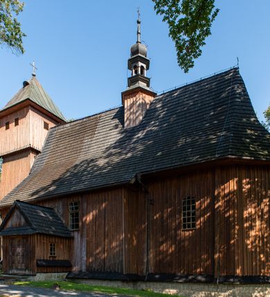 Zdjęcie nr 31: Kościół parafialny w Gruszowie znajduje się na niewielkim wzniesieniu w centrum miejscowości. Budowla jest orientowana, jednonawowa, z szerokim zamkniętym trójbocznie prezbiterium oraz czworoboczną wieżą od zachodu. Korpusu nawowy i prezbiterium charakteryzuje konstrukcja zrębowa, natomiast wieżę słupowa. Od północy do prezbiterium przylega zakrystia na rzucie prostokąta, natomiast do nawy zamknięta trójbocznie kaplica boczna. Do wnętrza kościoła prowadzą dwie kruchty, jedna od strony południowej, druga przez wieżę od zachodniej. Nad korpusem nawowym i prezbiterium znajduje się jednokalenicowy dach kryty gontem, a na styku nawy i prezbiterium usytuowana jest drewniana wieżyczka na sygnaturkę nakryta baniastym hełmem z latarnią. Zakrystia przekryta jest dachem pulpitowym, natomiast kaplica boczna oraz kruchty dachami dwuspadowymi krytymi gontem. Izbicową, o pochyłych ścianach wieżę wieńczy okuty blachą dach namiotowy. Elewacje osłania szalunek z pionowych desek z tzw. listwowaniem oraz pseudopilastry, dodatkowo wieżę w jednej trzeciej wysokości obiega niewielki parapet kryty gontem. W strukturze korpusu nawowego otwory okienne znajdują się po stronie południowej i mają kształt stojących prostokątów. W prezbiterium znajduje się po jednym oknie od południa i od wschodu, ich prostokątna forma jest zamknięta łukiem w ośli grzbiet. W kaplicy bocznej jest jedno okno od strony zachodniej. Ściana wschodnia zakrystii przepruta jest dwoma niewielkimi oknami, natomiast kruchty południowej jednym. W kruchcie zachodniej od południa jest jedno okno, natomiast w dolnej partii wieży znajdują się trzy, z czego dwa dolne oddziela od górnego niewielki daszek pulpitowy. Wnętrze korpusu nawowego i prezbiterium kościoła nakryte jest drewnianym stropem. Do kaplicy bocznej prowadzi szerokie przejście o ostrołukowym wykroju. Południowy portal w korpusie nawowym wieńczy wykrój w formie łuku w ośli grzbiet. Ściany i stropy wnętrza kościoła pokrywa secesyjna polichromia. 
Plac przykościelny otoczony jest drewnianym ogrodzeniem oraz starodrzewem.
