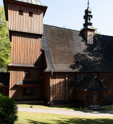 Zdjęcie nr 24: Kościół parafialny w Gruszowie znajduje się na niewielkim wzniesieniu w centrum miejscowości. Budowla jest orientowana, jednonawowa, z szerokim zamkniętym trójbocznie prezbiterium oraz czworoboczną wieżą od zachodu. Korpusu nawowy i prezbiterium charakteryzuje konstrukcja zrębowa, natomiast wieżę słupowa. Od północy do prezbiterium przylega zakrystia na rzucie prostokąta, natomiast do nawy zamknięta trójbocznie kaplica boczna. Do wnętrza kościoła prowadzą dwie kruchty, jedna od strony południowej, druga przez wieżę od zachodniej. Nad korpusem nawowym i prezbiterium znajduje się jednokalenicowy dach kryty gontem, a na styku nawy i prezbiterium usytuowana jest drewniana wieżyczka na sygnaturkę nakryta baniastym hełmem z latarnią. Zakrystia przekryta jest dachem pulpitowym, natomiast kaplica boczna oraz kruchty dachami dwuspadowymi krytymi gontem. Izbicową, o pochyłych ścianach wieżę wieńczy okuty blachą dach namiotowy. Elewacje osłania szalunek z pionowych desek z tzw. listwowaniem oraz pseudopilastry, dodatkowo wieżę w jednej trzeciej wysokości obiega niewielki parapet kryty gontem. W strukturze korpusu nawowego otwory okienne znajdują się po stronie południowej i mają kształt stojących prostokątów. W prezbiterium znajduje się po jednym oknie od południa i od wschodu, ich prostokątna forma jest zamknięta łukiem w ośli grzbiet. W kaplicy bocznej jest jedno okno od strony zachodniej. Ściana wschodnia zakrystii przepruta jest dwoma niewielkimi oknami, natomiast kruchty południowej jednym. W kruchcie zachodniej od południa jest jedno okno, natomiast w dolnej partii wieży znajdują się trzy, z czego dwa dolne oddziela od górnego niewielki daszek pulpitowy. Wnętrze korpusu nawowego i prezbiterium kościoła nakryte jest drewnianym stropem. Do kaplicy bocznej prowadzi szerokie przejście o ostrołukowym wykroju. Południowy portal w korpusie nawowym wieńczy wykrój w formie łuku w ośli grzbiet. Ściany i stropy wnętrza kościoła pokrywa secesyjna polichromia. 
Plac przykościelny otoczony jest drewnianym ogrodzeniem oraz starodrzewem.
