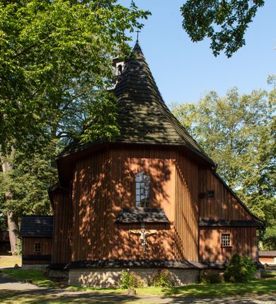 Zdjęcie nr 3: Kościół parafialny w Gruszowie znajduje się na niewielkim wzniesieniu w centrum miejscowości. Budowla jest orientowana, jednonawowa, z szerokim zamkniętym trójbocznie prezbiterium oraz czworoboczną wieżą od zachodu. Korpusu nawowy i prezbiterium charakteryzuje konstrukcja zrębowa, natomiast wieżę słupowa. Od północy do prezbiterium przylega zakrystia na rzucie prostokąta, natomiast do nawy zamknięta trójbocznie kaplica boczna. Do wnętrza kościoła prowadzą dwie kruchty, jedna od strony południowej, druga przez wieżę od zachodniej. Nad korpusem nawowym i prezbiterium znajduje się jednokalenicowy dach kryty gontem, a na styku nawy i prezbiterium usytuowana jest drewniana wieżyczka na sygnaturkę nakryta baniastym hełmem z latarnią. Zakrystia przekryta jest dachem pulpitowym, natomiast kaplica boczna oraz kruchty dachami dwuspadowymi krytymi gontem. Izbicową, o pochyłych ścianach wieżę wieńczy okuty blachą dach namiotowy. Elewacje osłania szalunek z pionowych desek z tzw. listwowaniem oraz pseudopilastry, dodatkowo wieżę w jednej trzeciej wysokości obiega niewielki parapet kryty gontem. W strukturze korpusu nawowego otwory okienne znajdują się po stronie południowej i mają kształt stojących prostokątów. W prezbiterium znajduje się po jednym oknie od południa i od wschodu, ich prostokątna forma jest zamknięta łukiem w ośli grzbiet. W kaplicy bocznej jest jedno okno od strony zachodniej. Ściana wschodnia zakrystii przepruta jest dwoma niewielkimi oknami, natomiast kruchty południowej jednym. W kruchcie zachodniej od południa jest jedno okno, natomiast w dolnej partii wieży znajdują się trzy, z czego dwa dolne oddziela od górnego niewielki daszek pulpitowy. Wnętrze korpusu nawowego i prezbiterium kościoła nakryte jest drewnianym stropem. Do kaplicy bocznej prowadzi szerokie przejście o ostrołukowym wykroju. Południowy portal w korpusie nawowym wieńczy wykrój w formie łuku w ośli grzbiet. Ściany i stropy wnętrza kościoła pokrywa secesyjna polichromia. 
Plac przykościelny otoczony jest drewnianym ogrodzeniem oraz starodrzewem.
