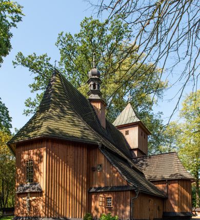 Zdjęcie nr 33: Kościół parafialny w Gruszowie znajduje się na niewielkim wzniesieniu w centrum miejscowości. Budowla jest orientowana, jednonawowa, z szerokim zamkniętym trójbocznie prezbiterium oraz czworoboczną wieżą od zachodu. Korpusu nawowy i prezbiterium charakteryzuje konstrukcja zrębowa, natomiast wieżę słupowa. Od północy do prezbiterium przylega zakrystia na rzucie prostokąta, natomiast do nawy zamknięta trójbocznie kaplica boczna. Do wnętrza kościoła prowadzą dwie kruchty, jedna od strony południowej, druga przez wieżę od zachodniej. Nad korpusem nawowym i prezbiterium znajduje się jednokalenicowy dach kryty gontem, a na styku nawy i prezbiterium usytuowana jest drewniana wieżyczka na sygnaturkę nakryta baniastym hełmem z latarnią. Zakrystia przekryta jest dachem pulpitowym, natomiast kaplica boczna oraz kruchty dachami dwuspadowymi krytymi gontem. Izbicową, o pochyłych ścianach wieżę wieńczy okuty blachą dach namiotowy. Elewacje osłania szalunek z pionowych desek z tzw. listwowaniem oraz pseudopilastry, dodatkowo wieżę w jednej trzeciej wysokości obiega niewielki parapet kryty gontem. W strukturze korpusu nawowego otwory okienne znajdują się po stronie południowej i mają kształt stojących prostokątów. W prezbiterium znajduje się po jednym oknie od południa i od wschodu, ich prostokątna forma jest zamknięta łukiem w ośli grzbiet. W kaplicy bocznej jest jedno okno od strony zachodniej. Ściana wschodnia zakrystii przepruta jest dwoma niewielkimi oknami, natomiast kruchty południowej jednym. W kruchcie zachodniej od południa jest jedno okno, natomiast w dolnej partii wieży znajdują się trzy, z czego dwa dolne oddziela od górnego niewielki daszek pulpitowy. Wnętrze korpusu nawowego i prezbiterium kościoła nakryte jest drewnianym stropem. Do kaplicy bocznej prowadzi szerokie przejście o ostrołukowym wykroju. Południowy portal w korpusie nawowym wieńczy wykrój w formie łuku w ośli grzbiet. Ściany i stropy wnętrza kościoła pokrywa secesyjna polichromia. 
Plac przykościelny otoczony jest drewnianym ogrodzeniem oraz starodrzewem.
