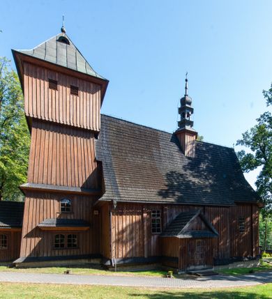 Zdjęcie nr 2: Kościół parafialny w Gruszowie znajduje się na niewielkim wzniesieniu w centrum miejscowości. Budowla jest orientowana, jednonawowa, z szerokim zamkniętym trójbocznie prezbiterium oraz czworoboczną wieżą od zachodu. Korpusu nawowy i prezbiterium charakteryzuje konstrukcja zrębowa, natomiast wieżę słupowa. Od północy do prezbiterium przylega zakrystia na rzucie prostokąta, natomiast do nawy zamknięta trójbocznie kaplica boczna. Do wnętrza kościoła prowadzą dwie kruchty, jedna od strony południowej, druga przez wieżę od zachodniej. Nad korpusem nawowym i prezbiterium znajduje się jednokalenicowy dach kryty gontem, a na styku nawy i prezbiterium usytuowana jest drewniana wieżyczka na sygnaturkę nakryta baniastym hełmem z latarnią. Zakrystia przekryta jest dachem pulpitowym, natomiast kaplica boczna oraz kruchty dachami dwuspadowymi krytymi gontem. Izbicową, o pochyłych ścianach wieżę wieńczy okuty blachą dach namiotowy. Elewacje osłania szalunek z pionowych desek z tzw. listwowaniem oraz pseudopilastry, dodatkowo wieżę w jednej trzeciej wysokości obiega niewielki parapet kryty gontem. W strukturze korpusu nawowego otwory okienne znajdują się po stronie południowej i mają kształt stojących prostokątów. W prezbiterium znajduje się po jednym oknie od południa i od wschodu, ich prostokątna forma jest zamknięta łukiem w ośli grzbiet. W kaplicy bocznej jest jedno okno od strony zachodniej. Ściana wschodnia zakrystii przepruta jest dwoma niewielkimi oknami, natomiast kruchty południowej jednym. W kruchcie zachodniej od południa jest jedno okno, natomiast w dolnej partii wieży znajdują się trzy, z czego dwa dolne oddziela od górnego niewielki daszek pulpitowy. Wnętrze korpusu nawowego i prezbiterium kościoła nakryte jest drewnianym stropem. Do kaplicy bocznej prowadzi szerokie przejście o ostrołukowym wykroju. Południowy portal w korpusie nawowym wieńczy wykrój w formie łuku w ośli grzbiet. Ściany i stropy wnętrza kościoła pokrywa secesyjna polichromia. 
Plac przykościelny otoczony jest drewnianym ogrodzeniem oraz starodrzewem.
