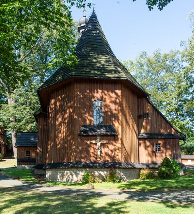 Zdjęcie nr 35: Kościół parafialny w Gruszowie znajduje się na niewielkim wzniesieniu w centrum miejscowości. Budowla jest orientowana, jednonawowa, z szerokim zamkniętym trójbocznie prezbiterium oraz czworoboczną wieżą od zachodu. Korpusu nawowy i prezbiterium charakteryzuje konstrukcja zrębowa, natomiast wieżę słupowa. Od północy do prezbiterium przylega zakrystia na rzucie prostokąta, natomiast do nawy zamknięta trójbocznie kaplica boczna. Do wnętrza kościoła prowadzą dwie kruchty, jedna od strony południowej, druga przez wieżę od zachodniej. Nad korpusem nawowym i prezbiterium znajduje się jednokalenicowy dach kryty gontem, a na styku nawy i prezbiterium usytuowana jest drewniana wieżyczka na sygnaturkę nakryta baniastym hełmem z latarnią. Zakrystia przekryta jest dachem pulpitowym, natomiast kaplica boczna oraz kruchty dachami dwuspadowymi krytymi gontem. Izbicową, o pochyłych ścianach wieżę wieńczy okuty blachą dach namiotowy. Elewacje osłania szalunek z pionowych desek z tzw. listwowaniem oraz pseudopilastry, dodatkowo wieżę w jednej trzeciej wysokości obiega niewielki parapet kryty gontem. W strukturze korpusu nawowego otwory okienne znajdują się po stronie południowej i mają kształt stojących prostokątów. W prezbiterium znajduje się po jednym oknie od południa i od wschodu, ich prostokątna forma jest zamknięta łukiem w ośli grzbiet. W kaplicy bocznej jest jedno okno od strony zachodniej. Ściana wschodnia zakrystii przepruta jest dwoma niewielkimi oknami, natomiast kruchty południowej jednym. W kruchcie zachodniej od południa jest jedno okno, natomiast w dolnej partii wieży znajdują się trzy, z czego dwa dolne oddziela od górnego niewielki daszek pulpitowy. Wnętrze korpusu nawowego i prezbiterium kościoła nakryte jest drewnianym stropem. Do kaplicy bocznej prowadzi szerokie przejście o ostrołukowym wykroju. Południowy portal w korpusie nawowym wieńczy wykrój w formie łuku w ośli grzbiet. Ściany i stropy wnętrza kościoła pokrywa secesyjna polichromia. 
Plac przykościelny otoczony jest drewnianym ogrodzeniem oraz starodrzewem.
