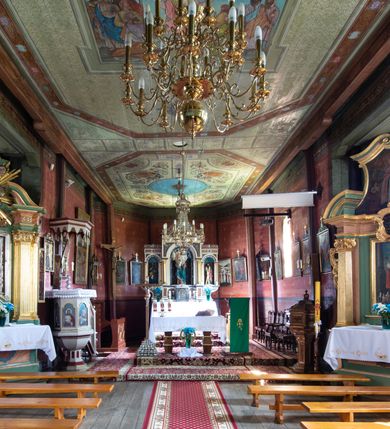 Zdjęcie nr 12: Kościół parafialny w Gruszowie znajduje się na niewielkim wzniesieniu w centrum miejscowości. Budowla jest orientowana, jednonawowa, z szerokim zamkniętym trójbocznie prezbiterium oraz czworoboczną wieżą od zachodu. Korpusu nawowy i prezbiterium charakteryzuje konstrukcja zrębowa, natomiast wieżę słupowa. Od północy do prezbiterium przylega zakrystia na rzucie prostokąta, natomiast do nawy zamknięta trójbocznie kaplica boczna. Do wnętrza kościoła prowadzą dwie kruchty, jedna od strony południowej, druga przez wieżę od zachodniej. Nad korpusem nawowym i prezbiterium znajduje się jednokalenicowy dach kryty gontem, a na styku nawy i prezbiterium usytuowana jest drewniana wieżyczka na sygnaturkę nakryta baniastym hełmem z latarnią. Zakrystia przekryta jest dachem pulpitowym, natomiast kaplica boczna oraz kruchty dachami dwuspadowymi krytymi gontem. Izbicową, o pochyłych ścianach wieżę wieńczy okuty blachą dach namiotowy. Elewacje osłania szalunek z pionowych desek z tzw. listwowaniem oraz pseudopilastry, dodatkowo wieżę w jednej trzeciej wysokości obiega niewielki parapet kryty gontem. W strukturze korpusu nawowego otwory okienne znajdują się po stronie południowej i mają kształt stojących prostokątów. W prezbiterium znajduje się po jednym oknie od południa i od wschodu, ich prostokątna forma jest zamknięta łukiem w ośli grzbiet. W kaplicy bocznej jest jedno okno od strony zachodniej. Ściana wschodnia zakrystii przepruta jest dwoma niewielkimi oknami, natomiast kruchty południowej jednym. W kruchcie zachodniej od południa jest jedno okno, natomiast w dolnej partii wieży znajdują się trzy, z czego dwa dolne oddziela od górnego niewielki daszek pulpitowy. Wnętrze korpusu nawowego i prezbiterium kościoła nakryte jest drewnianym stropem. Do kaplicy bocznej prowadzi szerokie przejście o ostrołukowym wykroju. Południowy portal w korpusie nawowym wieńczy wykrój w formie łuku w ośli grzbiet. Ściany i stropy wnętrza kościoła pokrywa secesyjna polichromia. 
Plac przykościelny otoczony jest drewnianym ogrodzeniem oraz starodrzewem.
