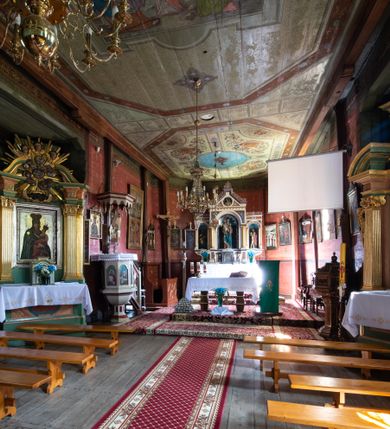 Zdjęcie nr 15: Kościół parafialny w Gruszowie znajduje się na niewielkim wzniesieniu w centrum miejscowości. Budowla jest orientowana, jednonawowa, z szerokim zamkniętym trójbocznie prezbiterium oraz czworoboczną wieżą od zachodu. Korpusu nawowy i prezbiterium charakteryzuje konstrukcja zrębowa, natomiast wieżę słupowa. Od północy do prezbiterium przylega zakrystia na rzucie prostokąta, natomiast do nawy zamknięta trójbocznie kaplica boczna. Do wnętrza kościoła prowadzą dwie kruchty, jedna od strony południowej, druga przez wieżę od zachodniej. Nad korpusem nawowym i prezbiterium znajduje się jednokalenicowy dach kryty gontem, a na styku nawy i prezbiterium usytuowana jest drewniana wieżyczka na sygnaturkę nakryta baniastym hełmem z latarnią. Zakrystia przekryta jest dachem pulpitowym, natomiast kaplica boczna oraz kruchty dachami dwuspadowymi krytymi gontem. Izbicową, o pochyłych ścianach wieżę wieńczy okuty blachą dach namiotowy. Elewacje osłania szalunek z pionowych desek z tzw. listwowaniem oraz pseudopilastry, dodatkowo wieżę w jednej trzeciej wysokości obiega niewielki parapet kryty gontem. W strukturze korpusu nawowego otwory okienne znajdują się po stronie południowej i mają kształt stojących prostokątów. W prezbiterium znajduje się po jednym oknie od południa i od wschodu, ich prostokątna forma jest zamknięta łukiem w ośli grzbiet. W kaplicy bocznej jest jedno okno od strony zachodniej. Ściana wschodnia zakrystii przepruta jest dwoma niewielkimi oknami, natomiast kruchty południowej jednym. W kruchcie zachodniej od południa jest jedno okno, natomiast w dolnej partii wieży znajdują się trzy, z czego dwa dolne oddziela od górnego niewielki daszek pulpitowy. Wnętrze korpusu nawowego i prezbiterium kościoła nakryte jest drewnianym stropem. Do kaplicy bocznej prowadzi szerokie przejście o ostrołukowym wykroju. Południowy portal w korpusie nawowym wieńczy wykrój w formie łuku w ośli grzbiet. Ściany i stropy wnętrza kościoła pokrywa secesyjna polichromia. 
Plac przykościelny otoczony jest drewnianym ogrodzeniem oraz starodrzewem.
