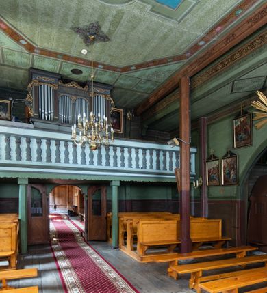 Zdjęcie nr 29: Kościół parafialny w Gruszowie znajduje się na niewielkim wzniesieniu w centrum miejscowości. Budowla jest orientowana, jednonawowa, z szerokim zamkniętym trójbocznie prezbiterium oraz czworoboczną wieżą od zachodu. Korpusu nawowy i prezbiterium charakteryzuje konstrukcja zrębowa, natomiast wieżę słupowa. Od północy do prezbiterium przylega zakrystia na rzucie prostokąta, natomiast do nawy zamknięta trójbocznie kaplica boczna. Do wnętrza kościoła prowadzą dwie kruchty, jedna od strony południowej, druga przez wieżę od zachodniej. Nad korpusem nawowym i prezbiterium znajduje się jednokalenicowy dach kryty gontem, a na styku nawy i prezbiterium usytuowana jest drewniana wieżyczka na sygnaturkę nakryta baniastym hełmem z latarnią. Zakrystia przekryta jest dachem pulpitowym, natomiast kaplica boczna oraz kruchty dachami dwuspadowymi krytymi gontem. Izbicową, o pochyłych ścianach wieżę wieńczy okuty blachą dach namiotowy. Elewacje osłania szalunek z pionowych desek z tzw. listwowaniem oraz pseudopilastry, dodatkowo wieżę w jednej trzeciej wysokości obiega niewielki parapet kryty gontem. W strukturze korpusu nawowego otwory okienne znajdują się po stronie południowej i mają kształt stojących prostokątów. W prezbiterium znajduje się po jednym oknie od południa i od wschodu, ich prostokątna forma jest zamknięta łukiem w ośli grzbiet. W kaplicy bocznej jest jedno okno od strony zachodniej. Ściana wschodnia zakrystii przepruta jest dwoma niewielkimi oknami, natomiast kruchty południowej jednym. W kruchcie zachodniej od południa jest jedno okno, natomiast w dolnej partii wieży znajdują się trzy, z czego dwa dolne oddziela od górnego niewielki daszek pulpitowy. Wnętrze korpusu nawowego i prezbiterium kościoła nakryte jest drewnianym stropem. Do kaplicy bocznej prowadzi szerokie przejście o ostrołukowym wykroju. Południowy portal w korpusie nawowym wieńczy wykrój w formie łuku w ośli grzbiet. Ściany i stropy wnętrza kościoła pokrywa secesyjna polichromia. 
Plac przykościelny otoczony jest drewnianym ogrodzeniem oraz starodrzewem.
