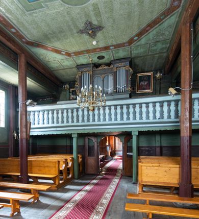 Zdjęcie nr 28: Kościół parafialny w Gruszowie znajduje się na niewielkim wzniesieniu w centrum miejscowości. Budowla jest orientowana, jednonawowa, z szerokim zamkniętym trójbocznie prezbiterium oraz czworoboczną wieżą od zachodu. Korpusu nawowy i prezbiterium charakteryzuje konstrukcja zrębowa, natomiast wieżę słupowa. Od północy do prezbiterium przylega zakrystia na rzucie prostokąta, natomiast do nawy zamknięta trójbocznie kaplica boczna. Do wnętrza kościoła prowadzą dwie kruchty, jedna od strony południowej, druga przez wieżę od zachodniej. Nad korpusem nawowym i prezbiterium znajduje się jednokalenicowy dach kryty gontem, a na styku nawy i prezbiterium usytuowana jest drewniana wieżyczka na sygnaturkę nakryta baniastym hełmem z latarnią. Zakrystia przekryta jest dachem pulpitowym, natomiast kaplica boczna oraz kruchty dachami dwuspadowymi krytymi gontem. Izbicową, o pochyłych ścianach wieżę wieńczy okuty blachą dach namiotowy. Elewacje osłania szalunek z pionowych desek z tzw. listwowaniem oraz pseudopilastry, dodatkowo wieżę w jednej trzeciej wysokości obiega niewielki parapet kryty gontem. W strukturze korpusu nawowego otwory okienne znajdują się po stronie południowej i mają kształt stojących prostokątów. W prezbiterium znajduje się po jednym oknie od południa i od wschodu, ich prostokątna forma jest zamknięta łukiem w ośli grzbiet. W kaplicy bocznej jest jedno okno od strony zachodniej. Ściana wschodnia zakrystii przepruta jest dwoma niewielkimi oknami, natomiast kruchty południowej jednym. W kruchcie zachodniej od południa jest jedno okno, natomiast w dolnej partii wieży znajdują się trzy, z czego dwa dolne oddziela od górnego niewielki daszek pulpitowy. Wnętrze korpusu nawowego i prezbiterium kościoła nakryte jest drewnianym stropem. Do kaplicy bocznej prowadzi szerokie przejście o ostrołukowym wykroju. Południowy portal w korpusie nawowym wieńczy wykrój w formie łuku w ośli grzbiet. Ściany i stropy wnętrza kościoła pokrywa secesyjna polichromia. 
Plac przykościelny otoczony jest drewnianym ogrodzeniem oraz starodrzewem.
