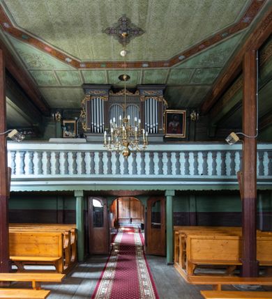 Zdjęcie nr 27: Kościół parafialny w Gruszowie znajduje się na niewielkim wzniesieniu w centrum miejscowości. Budowla jest orientowana, jednonawowa, z szerokim zamkniętym trójbocznie prezbiterium oraz czworoboczną wieżą od zachodu. Korpusu nawowy i prezbiterium charakteryzuje konstrukcja zrębowa, natomiast wieżę słupowa. Od północy do prezbiterium przylega zakrystia na rzucie prostokąta, natomiast do nawy zamknięta trójbocznie kaplica boczna. Do wnętrza kościoła prowadzą dwie kruchty, jedna od strony południowej, druga przez wieżę od zachodniej. Nad korpusem nawowym i prezbiterium znajduje się jednokalenicowy dach kryty gontem, a na styku nawy i prezbiterium usytuowana jest drewniana wieżyczka na sygnaturkę nakryta baniastym hełmem z latarnią. Zakrystia przekryta jest dachem pulpitowym, natomiast kaplica boczna oraz kruchty dachami dwuspadowymi krytymi gontem. Izbicową, o pochyłych ścianach wieżę wieńczy okuty blachą dach namiotowy. Elewacje osłania szalunek z pionowych desek z tzw. listwowaniem oraz pseudopilastry, dodatkowo wieżę w jednej trzeciej wysokości obiega niewielki parapet kryty gontem. W strukturze korpusu nawowego otwory okienne znajdują się po stronie południowej i mają kształt stojących prostokątów. W prezbiterium znajduje się po jednym oknie od południa i od wschodu, ich prostokątna forma jest zamknięta łukiem w ośli grzbiet. W kaplicy bocznej jest jedno okno od strony zachodniej. Ściana wschodnia zakrystii przepruta jest dwoma niewielkimi oknami, natomiast kruchty południowej jednym. W kruchcie zachodniej od południa jest jedno okno, natomiast w dolnej partii wieży znajdują się trzy, z czego dwa dolne oddziela od górnego niewielki daszek pulpitowy. Wnętrze korpusu nawowego i prezbiterium kościoła nakryte jest drewnianym stropem. Do kaplicy bocznej prowadzi szerokie przejście o ostrołukowym wykroju. Południowy portal w korpusie nawowym wieńczy wykrój w formie łuku w ośli grzbiet. Ściany i stropy wnętrza kościoła pokrywa secesyjna polichromia. 
Plac przykościelny otoczony jest drewnianym ogrodzeniem oraz starodrzewem.
