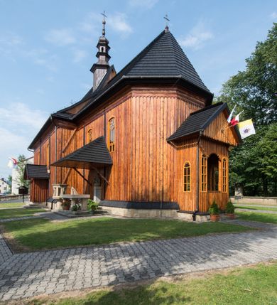 Zdjęcie nr 12: Kościół drewniany o konstrukcji zrębowej, elewacje jednolite, szalowane pionowo z listwowaniem, kruchta zachodnia o konstrukcji słupowo-ramowej. Więźba dachowa drewniana, krokwiowa. Budynek na kamiennym podmurowaniu przesłoniętym daszkiem gontowym. Kościół orientowany, jednonawowy, nawa na rzucie prostokąta, prezbiterium węższe, zakończone trójbocznie. Do wschodniej ściany prezbiterium przylega Ogrójec na rzucie prostokąta, od północy piętrowa zakrystia na planie prostokąta. Do południowej ściany nawy przylega niewielka kruchta na rzucie prostokąta oraz ołtarz polowy, od zachodu kruchta na planie prostokąta z węższym pięterkiem dzwonnym. Wnętrze podzielone lizenami, nakryte pułapami deskowymi. Pomiędzy nawą a prezbiterium prostokątny otwór tęczowy o zaokrąglonych narożach. Parapet chóru muzycznego w zachodniej części nawy podparty przez dwie kolumny o stylizowanych kapitelach. Otwory drzwiowe o prostokątnym wykroju w północnej ścianie prezbiterium, południowej i zachodniej nawy. Posadzka z płyt ceramicznych. Elewacja frontowa jednoosiowa. Na osi wejście do kruchty z dwuskrzydłowymi drzwiami, nakryte osobnym daszkiem dwuspadowym. Na północnej i południowej ścianie kruchty i pięterka dzwonnego niewielkie okna. Kruchta nakryta daszkiem trójspadowym gontowym, dzwonnica dwuspadowym, z krzyżem w partii szczytu. W elewacji południowej cztery otwory okienne w formie stojącego prostokąta zamkniętego łukiem półkolistym i odcinkowym, dwa w nawie i dwa w prezbiterium, w elewacji północnej dwa analogiczne otwory okienne. Na ścianie północnej zachowany fragment dawnych sobót, zabudowany pionowymi deskami. Na ścianie wschodniej prezbiterium Ogrójec w formie kapliczki przesłoniętej daszkiem dwuspadowym. Nawa nakryta dachem gontowym, dwuspadowym, półszczytowym, prezbiterium osobnym dachem wielospadowym, zakrystia przesłonięta dachem przyczółkowym, kruchta dwuspadowym, a ołtarz polowy trójspadowym. Nad nawą od strony prezbiterium wznosi się sześcioboczna wieżyczka na sygnaturkę z latarnią i hełmem cebulastym z kulą i krzyżem pokryta blachą. 



 
 
