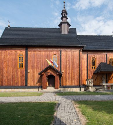 Zdjęcie nr 11: Kościół drewniany o konstrukcji zrębowej, elewacje jednolite, szalowane pionowo z listwowaniem, kruchta zachodnia o konstrukcji słupowo-ramowej. Więźba dachowa drewniana, krokwiowa. Budynek na kamiennym podmurowaniu przesłoniętym daszkiem gontowym. Kościół orientowany, jednonawowy, nawa na rzucie prostokąta, prezbiterium węższe, zakończone trójbocznie. Do wschodniej ściany prezbiterium przylega Ogrójec na rzucie prostokąta, od północy piętrowa zakrystia na planie prostokąta. Do południowej ściany nawy przylega niewielka kruchta na rzucie prostokąta oraz ołtarz polowy, od zachodu kruchta na planie prostokąta z węższym pięterkiem dzwonnym. Wnętrze podzielone lizenami, nakryte pułapami deskowymi. Pomiędzy nawą a prezbiterium prostokątny otwór tęczowy o zaokrąglonych narożach. Parapet chóru muzycznego w zachodniej części nawy podparty przez dwie kolumny o stylizowanych kapitelach. Otwory drzwiowe o prostokątnym wykroju w północnej ścianie prezbiterium, południowej i zachodniej nawy. Posadzka z płyt ceramicznych. Elewacja frontowa jednoosiowa. Na osi wejście do kruchty z dwuskrzydłowymi drzwiami, nakryte osobnym daszkiem dwuspadowym. Na północnej i południowej ścianie kruchty i pięterka dzwonnego niewielkie okna. Kruchta nakryta daszkiem trójspadowym gontowym, dzwonnica dwuspadowym, z krzyżem w partii szczytu. W elewacji południowej cztery otwory okienne w formie stojącego prostokąta zamkniętego łukiem półkolistym i odcinkowym, dwa w nawie i dwa w prezbiterium, w elewacji północnej dwa analogiczne otwory okienne. Na ścianie północnej zachowany fragment dawnych sobót, zabudowany pionowymi deskami. Na ścianie wschodniej prezbiterium Ogrójec w formie kapliczki przesłoniętej daszkiem dwuspadowym. Nawa nakryta dachem gontowym, dwuspadowym, półszczytowym, prezbiterium osobnym dachem wielospadowym, zakrystia przesłonięta dachem przyczółkowym, kruchta dwuspadowym, a ołtarz polowy trójspadowym. Nad nawą od strony prezbiterium wznosi się sześcioboczna wieżyczka na sygnaturkę z latarnią i hełmem cebulastym z kulą i krzyżem pokryta blachą. 



 
 
