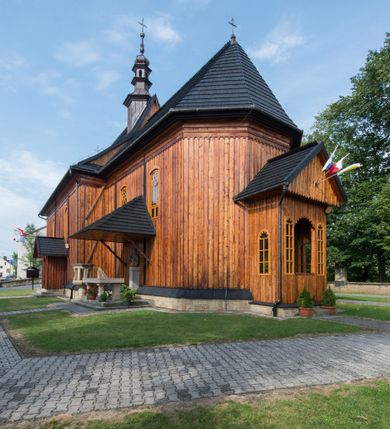 Zdjęcie nr 7: Kościół drewniany o konstrukcji zrębowej, elewacje jednolite, szalowane pionowo z listwowaniem, kruchta zachodnia o konstrukcji słupowo-ramowej. Więźba dachowa drewniana, krokwiowa. Budynek na kamiennym podmurowaniu przesłoniętym daszkiem gontowym. Kościół orientowany, jednonawowy, nawa na rzucie prostokąta, prezbiterium węższe, zakończone trójbocznie. Do wschodniej ściany prezbiterium przylega Ogrójec na rzucie prostokąta, od północy piętrowa zakrystia na planie prostokąta. Do południowej ściany nawy przylega niewielka kruchta na rzucie prostokąta oraz ołtarz polowy, od zachodu kruchta na planie prostokąta z węższym pięterkiem dzwonnym. Wnętrze podzielone lizenami, nakryte pułapami deskowymi. Pomiędzy nawą a prezbiterium prostokątny otwór tęczowy o zaokrąglonych narożach. Parapet chóru muzycznego w zachodniej części nawy podparty przez dwie kolumny o stylizowanych kapitelach. Otwory drzwiowe o prostokątnym wykroju w północnej ścianie prezbiterium, południowej i zachodniej nawy. Posadzka z płyt ceramicznych. Elewacja frontowa jednoosiowa. Na osi wejście do kruchty z dwuskrzydłowymi drzwiami, nakryte osobnym daszkiem dwuspadowym. Na północnej i południowej ścianie kruchty i pięterka dzwonnego niewielkie okna. Kruchta nakryta daszkiem trójspadowym gontowym, dzwonnica dwuspadowym, z krzyżem w partii szczytu. W elewacji południowej cztery otwory okienne w formie stojącego prostokąta zamkniętego łukiem półkolistym i odcinkowym, dwa w nawie i dwa w prezbiterium, w elewacji północnej dwa analogiczne otwory okienne. Na ścianie północnej zachowany fragment dawnych sobót, zabudowany pionowymi deskami. Na ścianie wschodniej prezbiterium Ogrójec w formie kapliczki przesłoniętej daszkiem dwuspadowym. Nawa nakryta dachem gontowym, dwuspadowym, półszczytowym, prezbiterium osobnym dachem wielospadowym, zakrystia przesłonięta dachem przyczółkowym, kruchta dwuspadowym, a ołtarz polowy trójspadowym. Nad nawą od strony prezbiterium wznosi się sześcioboczna wieżyczka na sygnaturkę z latarnią i hełmem cebulastym z kulą i krzyżem pokryta blachą. 



 
 
