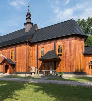 Zdjęcie nr 10: Kościół drewniany o konstrukcji zrębowej, elewacje jednolite, szalowane pionowo z listwowaniem, kruchta zachodnia o konstrukcji słupowo-ramowej. Więźba dachowa drewniana, krokwiowa. Budynek na kamiennym podmurowaniu przesłoniętym daszkiem gontowym. Kościół orientowany, jednonawowy, nawa na rzucie prostokąta, prezbiterium węższe, zakończone trójbocznie. Do wschodniej ściany prezbiterium przylega Ogrójec na rzucie prostokąta, od północy piętrowa zakrystia na planie prostokąta. Do południowej ściany nawy przylega niewielka kruchta na rzucie prostokąta oraz ołtarz polowy, od zachodu kruchta na planie prostokąta z węższym pięterkiem dzwonnym. Wnętrze podzielone lizenami, nakryte pułapami deskowymi. Pomiędzy nawą a prezbiterium prostokątny otwór tęczowy o zaokrąglonych narożach. Parapet chóru muzycznego w zachodniej części nawy podparty przez dwie kolumny o stylizowanych kapitelach. Otwory drzwiowe o prostokątnym wykroju w północnej ścianie prezbiterium, południowej i zachodniej nawy. Posadzka z płyt ceramicznych. Elewacja frontowa jednoosiowa. Na osi wejście do kruchty z dwuskrzydłowymi drzwiami, nakryte osobnym daszkiem dwuspadowym. Na północnej i południowej ścianie kruchty i pięterka dzwonnego niewielkie okna. Kruchta nakryta daszkiem trójspadowym gontowym, dzwonnica dwuspadowym, z krzyżem w partii szczytu. W elewacji południowej cztery otwory okienne w formie stojącego prostokąta zamkniętego łukiem półkolistym i odcinkowym, dwa w nawie i dwa w prezbiterium, w elewacji północnej dwa analogiczne otwory okienne. Na ścianie północnej zachowany fragment dawnych sobót, zabudowany pionowymi deskami. Na ścianie wschodniej prezbiterium Ogrójec w formie kapliczki przesłoniętej daszkiem dwuspadowym. Nawa nakryta dachem gontowym, dwuspadowym, półszczytowym, prezbiterium osobnym dachem wielospadowym, zakrystia przesłonięta dachem przyczółkowym, kruchta dwuspadowym, a ołtarz polowy trójspadowym. Nad nawą od strony prezbiterium wznosi się sześcioboczna wieżyczka na sygnaturkę z latarnią i hełmem cebulastym z kulą i krzyżem pokryta blachą. 



 
 
