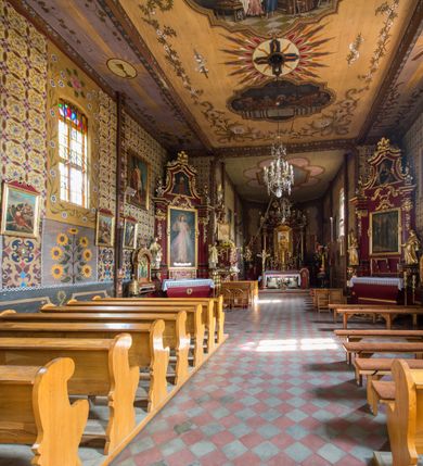 Zdjęcie nr 21: Kościół drewniany o konstrukcji zrębowej, elewacje jednolite, szalowane pionowo z listwowaniem, kruchta zachodnia o konstrukcji słupowo-ramowej. Więźba dachowa drewniana, krokwiowa. Budynek na kamiennym podmurowaniu przesłoniętym daszkiem gontowym. Kościół orientowany, jednonawowy, nawa na rzucie prostokąta, prezbiterium węższe, zakończone trójbocznie. Do wschodniej ściany prezbiterium przylega Ogrójec na rzucie prostokąta, od północy piętrowa zakrystia na planie prostokąta. Do południowej ściany nawy przylega niewielka kruchta na rzucie prostokąta oraz ołtarz polowy, od zachodu kruchta na planie prostokąta z węższym pięterkiem dzwonnym. Wnętrze podzielone lizenami, nakryte pułapami deskowymi. Pomiędzy nawą a prezbiterium prostokątny otwór tęczowy o zaokrąglonych narożach. Parapet chóru muzycznego w zachodniej części nawy podparty przez dwie kolumny o stylizowanych kapitelach. Otwory drzwiowe o prostokątnym wykroju w północnej ścianie prezbiterium, południowej i zachodniej nawy. Posadzka z płyt ceramicznych. Elewacja frontowa jednoosiowa. Na osi wejście do kruchty z dwuskrzydłowymi drzwiami, nakryte osobnym daszkiem dwuspadowym. Na północnej i południowej ścianie kruchty i pięterka dzwonnego niewielkie okna. Kruchta nakryta daszkiem trójspadowym gontowym, dzwonnica dwuspadowym, z krzyżem w partii szczytu. W elewacji południowej cztery otwory okienne w formie stojącego prostokąta zamkniętego łukiem półkolistym i odcinkowym, dwa w nawie i dwa w prezbiterium, w elewacji północnej dwa analogiczne otwory okienne. Na ścianie północnej zachowany fragment dawnych sobót, zabudowany pionowymi deskami. Na ścianie wschodniej prezbiterium Ogrójec w formie kapliczki przesłoniętej daszkiem dwuspadowym. Nawa nakryta dachem gontowym, dwuspadowym, półszczytowym, prezbiterium osobnym dachem wielospadowym, zakrystia przesłonięta dachem przyczółkowym, kruchta dwuspadowym, a ołtarz polowy trójspadowym. Nad nawą od strony prezbiterium wznosi się sześcioboczna wieżyczka na sygnaturkę z latarnią i hełmem cebulastym z kulą i krzyżem pokryta blachą. 



 
 
