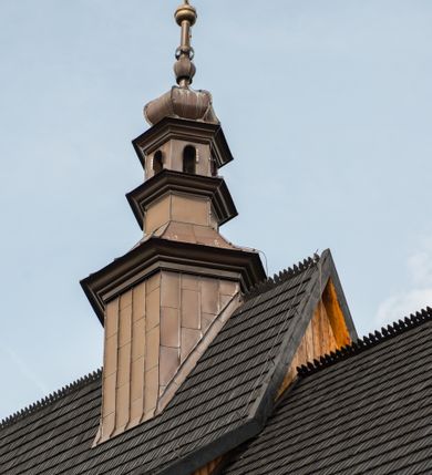 Zdjęcie nr 16: Kościół drewniany o konstrukcji zrębowej, elewacje jednolite, szalowane pionowo z listwowaniem, kruchta zachodnia o konstrukcji słupowo-ramowej. Więźba dachowa drewniana, krokwiowa. Budynek na kamiennym podmurowaniu przesłoniętym daszkiem gontowym. Kościół orientowany, jednonawowy, nawa na rzucie prostokąta, prezbiterium węższe, zakończone trójbocznie. Do wschodniej ściany prezbiterium przylega Ogrójec na rzucie prostokąta, od północy piętrowa zakrystia na planie prostokąta. Do południowej ściany nawy przylega niewielka kruchta na rzucie prostokąta oraz ołtarz polowy, od zachodu kruchta na planie prostokąta z węższym pięterkiem dzwonnym. Wnętrze podzielone lizenami, nakryte pułapami deskowymi. Pomiędzy nawą a prezbiterium prostokątny otwór tęczowy o zaokrąglonych narożach. Parapet chóru muzycznego w zachodniej części nawy podparty przez dwie kolumny o stylizowanych kapitelach. Otwory drzwiowe o prostokątnym wykroju w północnej ścianie prezbiterium, południowej i zachodniej nawy. Posadzka z płyt ceramicznych. Elewacja frontowa jednoosiowa. Na osi wejście do kruchty z dwuskrzydłowymi drzwiami, nakryte osobnym daszkiem dwuspadowym. Na północnej i południowej ścianie kruchty i pięterka dzwonnego niewielkie okna. Kruchta nakryta daszkiem trójspadowym gontowym, dzwonnica dwuspadowym, z krzyżem w partii szczytu. W elewacji południowej cztery otwory okienne w formie stojącego prostokąta zamkniętego łukiem półkolistym i odcinkowym, dwa w nawie i dwa w prezbiterium, w elewacji północnej dwa analogiczne otwory okienne. Na ścianie północnej zachowany fragment dawnych sobót, zabudowany pionowymi deskami. Na ścianie wschodniej prezbiterium Ogrójec w formie kapliczki przesłoniętej daszkiem dwuspadowym. Nawa nakryta dachem gontowym, dwuspadowym, półszczytowym, prezbiterium osobnym dachem wielospadowym, zakrystia przesłonięta dachem przyczółkowym, kruchta dwuspadowym, a ołtarz polowy trójspadowym. Nad nawą od strony prezbiterium wznosi się sześcioboczna wieżyczka na sygnaturkę z latarnią i hełmem cebulastym z kulą i krzyżem pokryta blachą. 



 
 
