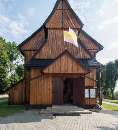 Zdjęcie nr 4: Kościół drewniany o konstrukcji zrębowej, elewacje jednolite, szalowane pionowo z listwowaniem, kruchta zachodnia o konstrukcji słupowo-ramowej. Więźba dachowa drewniana, krokwiowa. Budynek na kamiennym podmurowaniu przesłoniętym daszkiem gontowym. Kościół orientowany, jednonawowy, nawa na rzucie prostokąta, prezbiterium węższe, zakończone trójbocznie. Do wschodniej ściany prezbiterium przylega Ogrójec na rzucie prostokąta, od północy piętrowa zakrystia na planie prostokąta. Do południowej ściany nawy przylega niewielka kruchta na rzucie prostokąta oraz ołtarz polowy, od zachodu kruchta na planie prostokąta z węższym pięterkiem dzwonnym. Wnętrze podzielone lizenami, nakryte pułapami deskowymi. Pomiędzy nawą a prezbiterium prostokątny otwór tęczowy o zaokrąglonych narożach. Parapet chóru muzycznego w zachodniej części nawy podparty przez dwie kolumny o stylizowanych kapitelach. Otwory drzwiowe o prostokątnym wykroju w północnej ścianie prezbiterium, południowej i zachodniej nawy. Posadzka z płyt ceramicznych. Elewacja frontowa jednoosiowa. Na osi wejście do kruchty z dwuskrzydłowymi drzwiami, nakryte osobnym daszkiem dwuspadowym. Na północnej i południowej ścianie kruchty i pięterka dzwonnego niewielkie okna. Kruchta nakryta daszkiem trójspadowym gontowym, dzwonnica dwuspadowym, z krzyżem w partii szczytu. W elewacji południowej cztery otwory okienne w formie stojącego prostokąta zamkniętego łukiem półkolistym i odcinkowym, dwa w nawie i dwa w prezbiterium, w elewacji północnej dwa analogiczne otwory okienne. Na ścianie północnej zachowany fragment dawnych sobót, zabudowany pionowymi deskami. Na ścianie wschodniej prezbiterium Ogrójec w formie kapliczki przesłoniętej daszkiem dwuspadowym. Nawa nakryta dachem gontowym, dwuspadowym, półszczytowym, prezbiterium osobnym dachem wielospadowym, zakrystia przesłonięta dachem przyczółkowym, kruchta dwuspadowym, a ołtarz polowy trójspadowym. Nad nawą od strony prezbiterium wznosi się sześcioboczna wieżyczka na sygnaturkę z latarnią i hełmem cebulastym z kulą i krzyżem pokryta blachą. 



 
 
