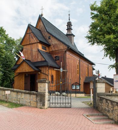 Zdjęcie nr 2: Kościół drewniany o konstrukcji zrębowej, elewacje jednolite, szalowane pionowo z listwowaniem, kruchta zachodnia o konstrukcji słupowo-ramowej. Więźba dachowa drewniana, krokwiowa. Budynek na kamiennym podmurowaniu przesłoniętym daszkiem gontowym. Kościół orientowany, jednonawowy, nawa na rzucie prostokąta, prezbiterium węższe, zakończone trójbocznie. Do wschodniej ściany prezbiterium przylega Ogrójec na rzucie prostokąta, od północy piętrowa zakrystia na planie prostokąta. Do południowej ściany nawy przylega niewielka kruchta na rzucie prostokąta oraz ołtarz polowy, od zachodu kruchta na planie prostokąta z węższym pięterkiem dzwonnym. Wnętrze podzielone lizenami, nakryte pułapami deskowymi. Pomiędzy nawą a prezbiterium prostokątny otwór tęczowy o zaokrąglonych narożach. Parapet chóru muzycznego w zachodniej części nawy podparty przez dwie kolumny o stylizowanych kapitelach. Otwory drzwiowe o prostokątnym wykroju w północnej ścianie prezbiterium, południowej i zachodniej nawy. Posadzka z płyt ceramicznych. Elewacja frontowa jednoosiowa. Na osi wejście do kruchty z dwuskrzydłowymi drzwiami, nakryte osobnym daszkiem dwuspadowym. Na północnej i południowej ścianie kruchty i pięterka dzwonnego niewielkie okna. Kruchta nakryta daszkiem trójspadowym gontowym, dzwonnica dwuspadowym, z krzyżem w partii szczytu. W elewacji południowej cztery otwory okienne w formie stojącego prostokąta zamkniętego łukiem półkolistym i odcinkowym, dwa w nawie i dwa w prezbiterium, w elewacji północnej dwa analogiczne otwory okienne. Na ścianie północnej zachowany fragment dawnych sobót, zabudowany pionowymi deskami. Na ścianie wschodniej prezbiterium Ogrójec w formie kapliczki przesłoniętej daszkiem dwuspadowym. Nawa nakryta dachem gontowym, dwuspadowym, półszczytowym, prezbiterium osobnym dachem wielospadowym, zakrystia przesłonięta dachem przyczółkowym, kruchta dwuspadowym, a ołtarz polowy trójspadowym. Nad nawą od strony prezbiterium wznosi się sześcioboczna wieżyczka na sygnaturkę z latarnią i hełmem cebulastym z kulą i krzyżem pokryta blachą. 



 
 
