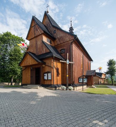 Zdjęcie nr 6: Kościół drewniany o konstrukcji zrębowej, elewacje jednolite, szalowane pionowo z listwowaniem, kruchta zachodnia o konstrukcji słupowo-ramowej. Więźba dachowa drewniana, krokwiowa. Budynek na kamiennym podmurowaniu przesłoniętym daszkiem gontowym. Kościół orientowany, jednonawowy, nawa na rzucie prostokąta, prezbiterium węższe, zakończone trójbocznie. Do wschodniej ściany prezbiterium przylega Ogrójec na rzucie prostokąta, od północy piętrowa zakrystia na planie prostokąta. Do południowej ściany nawy przylega niewielka kruchta na rzucie prostokąta oraz ołtarz polowy, od zachodu kruchta na planie prostokąta z węższym pięterkiem dzwonnym. Wnętrze podzielone lizenami, nakryte pułapami deskowymi. Pomiędzy nawą a prezbiterium prostokątny otwór tęczowy o zaokrąglonych narożach. Parapet chóru muzycznego w zachodniej części nawy podparty przez dwie kolumny o stylizowanych kapitelach. Otwory drzwiowe o prostokątnym wykroju w północnej ścianie prezbiterium, południowej i zachodniej nawy. Posadzka z płyt ceramicznych. Elewacja frontowa jednoosiowa. Na osi wejście do kruchty z dwuskrzydłowymi drzwiami, nakryte osobnym daszkiem dwuspadowym. Na północnej i południowej ścianie kruchty i pięterka dzwonnego niewielkie okna. Kruchta nakryta daszkiem trójspadowym gontowym, dzwonnica dwuspadowym, z krzyżem w partii szczytu. W elewacji południowej cztery otwory okienne w formie stojącego prostokąta zamkniętego łukiem półkolistym i odcinkowym, dwa w nawie i dwa w prezbiterium, w elewacji północnej dwa analogiczne otwory okienne. Na ścianie północnej zachowany fragment dawnych sobót, zabudowany pionowymi deskami. Na ścianie wschodniej prezbiterium Ogrójec w formie kapliczki przesłoniętej daszkiem dwuspadowym. Nawa nakryta dachem gontowym, dwuspadowym, półszczytowym, prezbiterium osobnym dachem wielospadowym, zakrystia przesłonięta dachem przyczółkowym, kruchta dwuspadowym, a ołtarz polowy trójspadowym. Nad nawą od strony prezbiterium wznosi się sześcioboczna wieżyczka na sygnaturkę z latarnią i hełmem cebulastym z kulą i krzyżem pokryta blachą. 



 
 
