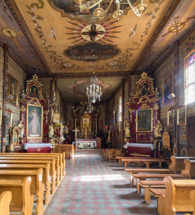 Zdjęcie nr 19: Kościół drewniany o konstrukcji zrębowej, elewacje jednolite, szalowane pionowo z listwowaniem, kruchta zachodnia o konstrukcji słupowo-ramowej. Więźba dachowa drewniana, krokwiowa. Budynek na kamiennym podmurowaniu przesłoniętym daszkiem gontowym. Kościół orientowany, jednonawowy, nawa na rzucie prostokąta, prezbiterium węższe, zakończone trójbocznie. Do wschodniej ściany prezbiterium przylega Ogrójec na rzucie prostokąta, od północy piętrowa zakrystia na planie prostokąta. Do południowej ściany nawy przylega niewielka kruchta na rzucie prostokąta oraz ołtarz polowy, od zachodu kruchta na planie prostokąta z węższym pięterkiem dzwonnym. Wnętrze podzielone lizenami, nakryte pułapami deskowymi. Pomiędzy nawą a prezbiterium prostokątny otwór tęczowy o zaokrąglonych narożach. Parapet chóru muzycznego w zachodniej części nawy podparty przez dwie kolumny o stylizowanych kapitelach. Otwory drzwiowe o prostokątnym wykroju w północnej ścianie prezbiterium, południowej i zachodniej nawy. Posadzka z płyt ceramicznych. Elewacja frontowa jednoosiowa. Na osi wejście do kruchty z dwuskrzydłowymi drzwiami, nakryte osobnym daszkiem dwuspadowym. Na północnej i południowej ścianie kruchty i pięterka dzwonnego niewielkie okna. Kruchta nakryta daszkiem trójspadowym gontowym, dzwonnica dwuspadowym, z krzyżem w partii szczytu. W elewacji południowej cztery otwory okienne w formie stojącego prostokąta zamkniętego łukiem półkolistym i odcinkowym, dwa w nawie i dwa w prezbiterium, w elewacji północnej dwa analogiczne otwory okienne. Na ścianie północnej zachowany fragment dawnych sobót, zabudowany pionowymi deskami. Na ścianie wschodniej prezbiterium Ogrójec w formie kapliczki przesłoniętej daszkiem dwuspadowym. Nawa nakryta dachem gontowym, dwuspadowym, półszczytowym, prezbiterium osobnym dachem wielospadowym, zakrystia przesłonięta dachem przyczółkowym, kruchta dwuspadowym, a ołtarz polowy trójspadowym. Nad nawą od strony prezbiterium wznosi się sześcioboczna wieżyczka na sygnaturkę z latarnią i hełmem cebulastym z kulą i krzyżem pokryta blachą. 



 
 
