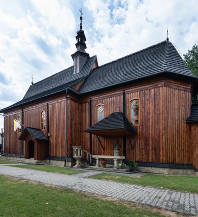 Zdjęcie nr 9: Kościół drewniany o konstrukcji zrębowej, elewacje jednolite, szalowane pionowo z listwowaniem, kruchta zachodnia o konstrukcji słupowo-ramowej. Więźba dachowa drewniana, krokwiowa. Budynek na kamiennym podmurowaniu przesłoniętym daszkiem gontowym. Kościół orientowany, jednonawowy, nawa na rzucie prostokąta, prezbiterium węższe, zakończone trójbocznie. Do wschodniej ściany prezbiterium przylega Ogrójec na rzucie prostokąta, od północy piętrowa zakrystia na planie prostokąta. Do południowej ściany nawy przylega niewielka kruchta na rzucie prostokąta oraz ołtarz polowy, od zachodu kruchta na planie prostokąta z węższym pięterkiem dzwonnym. Wnętrze podzielone lizenami, nakryte pułapami deskowymi. Pomiędzy nawą a prezbiterium prostokątny otwór tęczowy o zaokrąglonych narożach. Parapet chóru muzycznego w zachodniej części nawy podparty przez dwie kolumny o stylizowanych kapitelach. Otwory drzwiowe o prostokątnym wykroju w północnej ścianie prezbiterium, południowej i zachodniej nawy. Posadzka z płyt ceramicznych. Elewacja frontowa jednoosiowa. Na osi wejście do kruchty z dwuskrzydłowymi drzwiami, nakryte osobnym daszkiem dwuspadowym. Na północnej i południowej ścianie kruchty i pięterka dzwonnego niewielkie okna. Kruchta nakryta daszkiem trójspadowym gontowym, dzwonnica dwuspadowym, z krzyżem w partii szczytu. W elewacji południowej cztery otwory okienne w formie stojącego prostokąta zamkniętego łukiem półkolistym i odcinkowym, dwa w nawie i dwa w prezbiterium, w elewacji północnej dwa analogiczne otwory okienne. Na ścianie północnej zachowany fragment dawnych sobót, zabudowany pionowymi deskami. Na ścianie wschodniej prezbiterium Ogrójec w formie kapliczki przesłoniętej daszkiem dwuspadowym. Nawa nakryta dachem gontowym, dwuspadowym, półszczytowym, prezbiterium osobnym dachem wielospadowym, zakrystia przesłonięta dachem przyczółkowym, kruchta dwuspadowym, a ołtarz polowy trójspadowym. Nad nawą od strony prezbiterium wznosi się sześcioboczna wieżyczka na sygnaturkę z latarnią i hełmem cebulastym z kulą i krzyżem pokryta blachą. 



 
 
