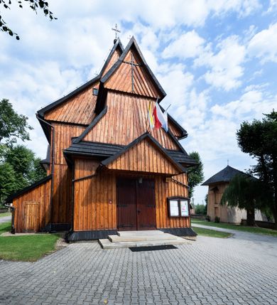 Zdjęcie nr 5: Kościół drewniany o konstrukcji zrębowej, elewacje jednolite, szalowane pionowo z listwowaniem, kruchta zachodnia o konstrukcji słupowo-ramowej. Więźba dachowa drewniana, krokwiowa. Budynek na kamiennym podmurowaniu przesłoniętym daszkiem gontowym. Kościół orientowany, jednonawowy, nawa na rzucie prostokąta, prezbiterium węższe, zakończone trójbocznie. Do wschodniej ściany prezbiterium przylega Ogrójec na rzucie prostokąta, od północy piętrowa zakrystia na planie prostokąta. Do południowej ściany nawy przylega niewielka kruchta na rzucie prostokąta oraz ołtarz polowy, od zachodu kruchta na planie prostokąta z węższym pięterkiem dzwonnym. Wnętrze podzielone lizenami, nakryte pułapami deskowymi. Pomiędzy nawą a prezbiterium prostokątny otwór tęczowy o zaokrąglonych narożach. Parapet chóru muzycznego w zachodniej części nawy podparty przez dwie kolumny o stylizowanych kapitelach. Otwory drzwiowe o prostokątnym wykroju w północnej ścianie prezbiterium, południowej i zachodniej nawy. Posadzka z płyt ceramicznych. Elewacja frontowa jednoosiowa. Na osi wejście do kruchty z dwuskrzydłowymi drzwiami, nakryte osobnym daszkiem dwuspadowym. Na północnej i południowej ścianie kruchty i pięterka dzwonnego niewielkie okna. Kruchta nakryta daszkiem trójspadowym gontowym, dzwonnica dwuspadowym, z krzyżem w partii szczytu. W elewacji południowej cztery otwory okienne w formie stojącego prostokąta zamkniętego łukiem półkolistym i odcinkowym, dwa w nawie i dwa w prezbiterium, w elewacji północnej dwa analogiczne otwory okienne. Na ścianie północnej zachowany fragment dawnych sobót, zabudowany pionowymi deskami. Na ścianie wschodniej prezbiterium Ogrójec w formie kapliczki przesłoniętej daszkiem dwuspadowym. Nawa nakryta dachem gontowym, dwuspadowym, półszczytowym, prezbiterium osobnym dachem wielospadowym, zakrystia przesłonięta dachem przyczółkowym, kruchta dwuspadowym, a ołtarz polowy trójspadowym. Nad nawą od strony prezbiterium wznosi się sześcioboczna wieżyczka na sygnaturkę z latarnią i hełmem cebulastym z kulą i krzyżem pokryta blachą. 



 
 
