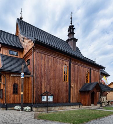 Zdjęcie nr 13: Kościół drewniany o konstrukcji zrębowej, elewacje jednolite, szalowane pionowo z listwowaniem, kruchta zachodnia o konstrukcji słupowo-ramowej. Więźba dachowa drewniana, krokwiowa. Budynek na kamiennym podmurowaniu przesłoniętym daszkiem gontowym. Kościół orientowany, jednonawowy, nawa na rzucie prostokąta, prezbiterium węższe, zakończone trójbocznie. Do wschodniej ściany prezbiterium przylega Ogrójec na rzucie prostokąta, od północy piętrowa zakrystia na planie prostokąta. Do południowej ściany nawy przylega niewielka kruchta na rzucie prostokąta oraz ołtarz polowy, od zachodu kruchta na planie prostokąta z węższym pięterkiem dzwonnym. Wnętrze podzielone lizenami, nakryte pułapami deskowymi. Pomiędzy nawą a prezbiterium prostokątny otwór tęczowy o zaokrąglonych narożach. Parapet chóru muzycznego w zachodniej części nawy podparty przez dwie kolumny o stylizowanych kapitelach. Otwory drzwiowe o prostokątnym wykroju w północnej ścianie prezbiterium, południowej i zachodniej nawy. Posadzka z płyt ceramicznych. Elewacja frontowa jednoosiowa. Na osi wejście do kruchty z dwuskrzydłowymi drzwiami, nakryte osobnym daszkiem dwuspadowym. Na północnej i południowej ścianie kruchty i pięterka dzwonnego niewielkie okna. Kruchta nakryta daszkiem trójspadowym gontowym, dzwonnica dwuspadowym, z krzyżem w partii szczytu. W elewacji południowej cztery otwory okienne w formie stojącego prostokąta zamkniętego łukiem półkolistym i odcinkowym, dwa w nawie i dwa w prezbiterium, w elewacji północnej dwa analogiczne otwory okienne. Na ścianie północnej zachowany fragment dawnych sobót, zabudowany pionowymi deskami. Na ścianie wschodniej prezbiterium Ogrójec w formie kapliczki przesłoniętej daszkiem dwuspadowym. Nawa nakryta dachem gontowym, dwuspadowym, półszczytowym, prezbiterium osobnym dachem wielospadowym, zakrystia przesłonięta dachem przyczółkowym, kruchta dwuspadowym, a ołtarz polowy trójspadowym. Nad nawą od strony prezbiterium wznosi się sześcioboczna wieżyczka na sygnaturkę z latarnią i hełmem cebulastym z kulą i krzyżem pokryta blachą. 



 
 
