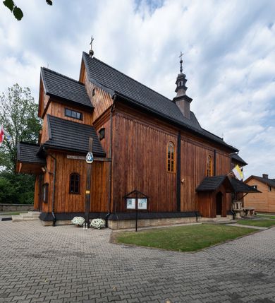 Zdjęcie nr 14: Kościół drewniany o konstrukcji zrębowej, elewacje jednolite, szalowane pionowo z listwowaniem, kruchta zachodnia o konstrukcji słupowo-ramowej. Więźba dachowa drewniana, krokwiowa. Budynek na kamiennym podmurowaniu przesłoniętym daszkiem gontowym. Kościół orientowany, jednonawowy, nawa na rzucie prostokąta, prezbiterium węższe, zakończone trójbocznie. Do wschodniej ściany prezbiterium przylega Ogrójec na rzucie prostokąta, od północy piętrowa zakrystia na planie prostokąta. Do południowej ściany nawy przylega niewielka kruchta na rzucie prostokąta oraz ołtarz polowy, od zachodu kruchta na planie prostokąta z węższym pięterkiem dzwonnym. Wnętrze podzielone lizenami, nakryte pułapami deskowymi. Pomiędzy nawą a prezbiterium prostokątny otwór tęczowy o zaokrąglonych narożach. Parapet chóru muzycznego w zachodniej części nawy podparty przez dwie kolumny o stylizowanych kapitelach. Otwory drzwiowe o prostokątnym wykroju w północnej ścianie prezbiterium, południowej i zachodniej nawy. Posadzka z płyt ceramicznych. Elewacja frontowa jednoosiowa. Na osi wejście do kruchty z dwuskrzydłowymi drzwiami, nakryte osobnym daszkiem dwuspadowym. Na północnej i południowej ścianie kruchty i pięterka dzwonnego niewielkie okna. Kruchta nakryta daszkiem trójspadowym gontowym, dzwonnica dwuspadowym, z krzyżem w partii szczytu. W elewacji południowej cztery otwory okienne w formie stojącego prostokąta zamkniętego łukiem półkolistym i odcinkowym, dwa w nawie i dwa w prezbiterium, w elewacji północnej dwa analogiczne otwory okienne. Na ścianie północnej zachowany fragment dawnych sobót, zabudowany pionowymi deskami. Na ścianie wschodniej prezbiterium Ogrójec w formie kapliczki przesłoniętej daszkiem dwuspadowym. Nawa nakryta dachem gontowym, dwuspadowym, półszczytowym, prezbiterium osobnym dachem wielospadowym, zakrystia przesłonięta dachem przyczółkowym, kruchta dwuspadowym, a ołtarz polowy trójspadowym. Nad nawą od strony prezbiterium wznosi się sześcioboczna wieżyczka na sygnaturkę z latarnią i hełmem cebulastym z kulą i krzyżem pokryta blachą. 



 
 
