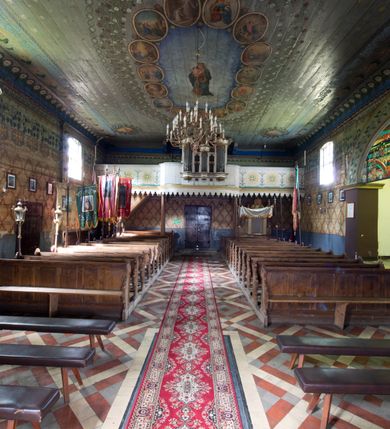 Zdjęcie nr 3: Chór muzyczny stanowi przyścienną, trójosiową, konstrukcję zawieszoną na dwóch kroksztynach i wspartą na dwóch smukłych kolumnach podtrzymujących oś środkową. Prowadzą na niego dwubiegowe schody w nawie ustawione od południa. Parapet chóru jest trójosiowy, wybrzuszony w osi środkowej, z silnie zaznaczonym, wyłamującym się cokołem i podwieszonym lambrekinem. W osiach bocznych parapet dekorują trzy malowane okręgi z przestylizowanym krzyżem wewnątrz, otoczonym potrójnymi promieniami pomiędzy ramionami, poprzedzielane smukłymi gałązkami kwiatów, z wyobrażeniem trawy poniżej. Prospekt jest pięcioosiowy, z osiami skrajnymi wyższymi od środkowej, podtrzymywany przez trzy konsolki z imitacją puklowania. Cokół wsparty na konsolach jest wyłamany na osiach skrajnych i wypukły w osi środkowej. Nisze na piszczałki są prostokątne. Siedem piszczałek ustawiono pod kątem. Zbiegają się  one ku środkowi. W górnej partii umieszczono ornament utworzony ze stylizowanej wici roślinnej. Powyżej znajduje się niepełne belkowanie, wyłamane analogicznie jak cokół, z pionowymi prześwitami, zwieńczone ornamentami roślinnymi i krzyżem pośrodku. Osie druga i czwarta są dwukondygnacyjne z prostokątnymi prześwitami na piszczałki, ze zwieńczeniami utworzonymi z ze stylizowanej wici roślinnej. Kolorystyka prospektu jest jasna, beżowa. Detale, cokoły i belkowania pierwotnie były złocone.
