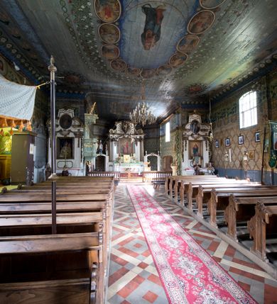 Zdjęcie nr 5: Kościół pw. św. Wawrzyńca w Grojcu jest drewnianą budowlą orientowaną, jednonawową z trójbocznie zamkniętym węższym prezbiterium od wschodu i wieżą od zachodu. Prostokątna nawa została wzniesiona na zrąb. Nawę i prezbiterium przykrywa dach siodłowy pokryty blachą cynkowaną. Do prezbiterium od północy przylega murowana zakrystia na rzucie prostokąta nakryta blaszanym dachem pulpitowym, a od południa prostokątny, drewniany aneks pełniący funkcję kaplicy bocznej, o podobnym dachu. Od północy do nawy dostawiono murowaną kaplicę na rzucie prostokąta przylegającą do zakrystii, a od południa niewielką czworoboczną kruchtę. Obie przestrzenie przykryto blaszanym dachem pulpitowym. W kruchcie południowej znajduje się drewniany portal z nadprożem w wykroju w ośli grzbiet. Nad wschodnią częścią nawy usytuowano sygnaturkę w kształcie wielobocznej latarni z krzyżem. Od zachodu do nawy dostawiono czworoboczną, drewnianą wieżę wzniesioną w konstrukcji słupowej, która w połowie nad nawą jest nadwieszona. Jej ściany są pionowe podzielone daszkami na trzy kondygnacje. Nakrywa ją blaszany, namiotowy hełm z latarnią zwieńczoną krzyżem. W przyziemiu wieży urządzono kruchtę. Wnętrze kościoła nakryto stropem z fasetą oddzieloną od ścian gzymsem. W zachodniej części nawy urządzono chór muzyczny zawieszony na dwóch kroksztynach i wsparty na kolumnach. W prezbiterium na ścianie wschodniej znajduje się ołtarz główny, a w nawie przy tęczy dwa ołtarze boczne oraz ambona.   