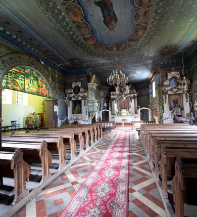 Zdjęcie nr 4: Kościół pw. św. Wawrzyńca w Grojcu jest drewnianą budowlą orientowaną, jednonawową z trójbocznie zamkniętym węższym prezbiterium od wschodu i wieżą od zachodu. Prostokątna nawa została wzniesiona na zrąb. Nawę i prezbiterium przykrywa dach siodłowy pokryty blachą cynkowaną. Do prezbiterium od północy przylega murowana zakrystia na rzucie prostokąta nakryta blaszanym dachem pulpitowym, a od południa prostokątny, drewniany aneks pełniący funkcję kaplicy bocznej, o podobnym dachu. Od północy do nawy dostawiono murowaną kaplicę na rzucie prostokąta przylegającą do zakrystii, a od południa niewielką czworoboczną kruchtę. Obie przestrzenie przykryto blaszanym dachem pulpitowym. W kruchcie południowej znajduje się drewniany portal z nadprożem w wykroju w ośli grzbiet. Nad wschodnią częścią nawy usytuowano sygnaturkę w kształcie wielobocznej latarni z krzyżem. Od zachodu do nawy dostawiono czworoboczną, drewnianą wieżę wzniesioną w konstrukcji słupowej, która w połowie nad nawą jest nadwieszona. Jej ściany są pionowe podzielone daszkami na trzy kondygnacje. Nakrywa ją blaszany, namiotowy hełm z latarnią zwieńczoną krzyżem. W przyziemiu wieży urządzono kruchtę. Wnętrze kościoła nakryto stropem z fasetą oddzieloną od ścian gzymsem. W zachodniej części nawy urządzono chór muzyczny zawieszony na dwóch kroksztynach i wsparty na kolumnach. W prezbiterium na ścianie wschodniej znajduje się ołtarz główny, a w nawie przy tęczy dwa ołtarze boczne oraz ambona.   