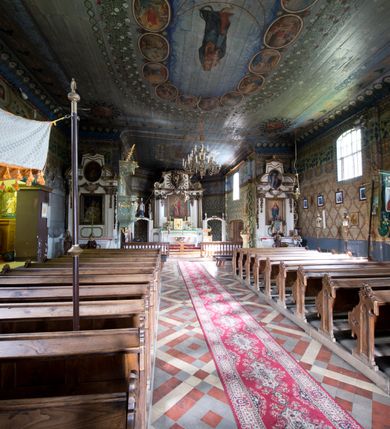 Zdjęcie nr 6: Kościół pw. św. Wawrzyńca w Grojcu jest drewnianą budowlą orientowaną, jednonawową z trójbocznie zamkniętym węższym prezbiterium od wschodu i wieżą od zachodu. Prostokątna nawa została wzniesiona na zrąb. Nawę i prezbiterium przykrywa dach siodłowy pokryty blachą cynkowaną. Do prezbiterium od północy przylega murowana zakrystia na rzucie prostokąta nakryta blaszanym dachem pulpitowym, a od południa prostokątny, drewniany aneks pełniący funkcję kaplicy bocznej, o podobnym dachu. Od północy do nawy dostawiono murowaną kaplicę na rzucie prostokąta przylegającą do zakrystii, a od południa niewielką czworoboczną kruchtę. Obie przestrzenie przykryto blaszanym dachem pulpitowym. W kruchcie południowej znajduje się drewniany portal z nadprożem w wykroju w ośli grzbiet. Nad wschodnią częścią nawy usytuowano sygnaturkę w kształcie wielobocznej latarni z krzyżem. Od zachodu do nawy dostawiono czworoboczną, drewnianą wieżę wzniesioną w konstrukcji słupowej, która w połowie nad nawą jest nadwieszona. Jej ściany są pionowe podzielone daszkami na trzy kondygnacje. Nakrywa ją blaszany, namiotowy hełm z latarnią zwieńczoną krzyżem. W przyziemiu wieży urządzono kruchtę. Wnętrze kościoła nakryto stropem z fasetą oddzieloną od ścian gzymsem. W zachodniej części nawy urządzono chór muzyczny zawieszony na dwóch kroksztynach i wsparty na kolumnach. W prezbiterium na ścianie wschodniej znajduje się ołtarz główny, a w nawie przy tęczy dwa ołtarze boczne oraz ambona.   