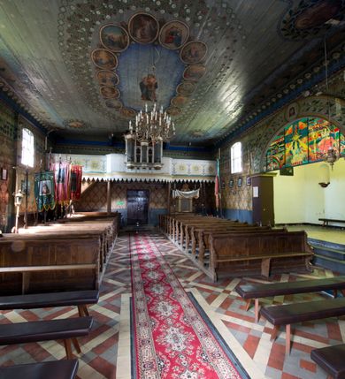 Zdjęcie nr 8: Kościół pw. św. Wawrzyńca w Grojcu jest drewnianą budowlą orientowaną, jednonawową z trójbocznie zamkniętym węższym prezbiterium od wschodu i wieżą od zachodu. Prostokątna nawa została wzniesiona na zrąb. Nawę i prezbiterium przykrywa dach siodłowy pokryty blachą cynkowaną. Do prezbiterium od północy przylega murowana zakrystia na rzucie prostokąta nakryta blaszanym dachem pulpitowym, a od południa prostokątny, drewniany aneks pełniący funkcję kaplicy bocznej, o podobnym dachu. Od północy do nawy dostawiono murowaną kaplicę na rzucie prostokąta przylegającą do zakrystii, a od południa niewielką czworoboczną kruchtę. Obie przestrzenie przykryto blaszanym dachem pulpitowym. W kruchcie południowej znajduje się drewniany portal z nadprożem w wykroju w ośli grzbiet. Nad wschodnią częścią nawy usytuowano sygnaturkę w kształcie wielobocznej latarni z krzyżem. Od zachodu do nawy dostawiono czworoboczną, drewnianą wieżę wzniesioną w konstrukcji słupowej, która w połowie nad nawą jest nadwieszona. Jej ściany są pionowe podzielone daszkami na trzy kondygnacje. Nakrywa ją blaszany, namiotowy hełm z latarnią zwieńczoną krzyżem. W przyziemiu wieży urządzono kruchtę. Wnętrze kościoła nakryto stropem z fasetą oddzieloną od ścian gzymsem. W zachodniej części nawy urządzono chór muzyczny zawieszony na dwóch kroksztynach i wsparty na kolumnach. W prezbiterium na ścianie wschodniej znajduje się ołtarz główny, a w nawie przy tęczy dwa ołtarze boczne oraz ambona.   