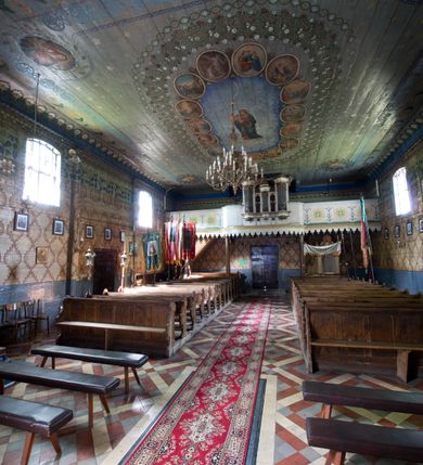 Zdjęcie nr 9: Kościół pw. św. Wawrzyńca w Grojcu jest drewnianą budowlą orientowaną, jednonawową z trójbocznie zamkniętym węższym prezbiterium od wschodu i wieżą od zachodu. Prostokątna nawa została wzniesiona na zrąb. Nawę i prezbiterium przykrywa dach siodłowy pokryty blachą cynkowaną. Do prezbiterium od północy przylega murowana zakrystia na rzucie prostokąta nakryta blaszanym dachem pulpitowym, a od południa prostokątny, drewniany aneks pełniący funkcję kaplicy bocznej, o podobnym dachu. Od północy do nawy dostawiono murowaną kaplicę na rzucie prostokąta przylegającą do zakrystii, a od południa niewielką czworoboczną kruchtę. Obie przestrzenie przykryto blaszanym dachem pulpitowym. W kruchcie południowej znajduje się drewniany portal z nadprożem w wykroju w ośli grzbiet. Nad wschodnią częścią nawy usytuowano sygnaturkę w kształcie wielobocznej latarni z krzyżem. Od zachodu do nawy dostawiono czworoboczną, drewnianą wieżę wzniesioną w konstrukcji słupowej, która w połowie nad nawą jest nadwieszona. Jej ściany są pionowe podzielone daszkami na trzy kondygnacje. Nakrywa ją blaszany, namiotowy hełm z latarnią zwieńczoną krzyżem. W przyziemiu wieży urządzono kruchtę. Wnętrze kościoła nakryto stropem z fasetą oddzieloną od ścian gzymsem. W zachodniej części nawy urządzono chór muzyczny zawieszony na dwóch kroksztynach i wsparty na kolumnach. W prezbiterium na ścianie wschodniej znajduje się ołtarz główny, a w nawie przy tęczy dwa ołtarze boczne oraz ambona.   