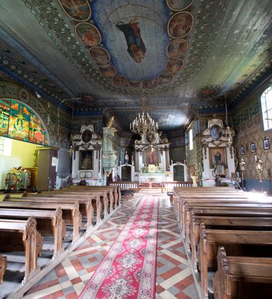 Zdjęcie nr 17: Kościół pw. św. Wawrzyńca w Grojcu jest drewnianą budowlą orientowaną, jednonawową z trójbocznie zamkniętym węższym prezbiterium od wschodu i wieżą od zachodu. Prostokątna nawa została wzniesiona na zrąb. Nawę i prezbiterium przykrywa dach siodłowy pokryty blachą cynkowaną. Do prezbiterium od północy przylega murowana zakrystia na rzucie prostokąta nakryta blaszanym dachem pulpitowym, a od południa prostokątny, drewniany aneks pełniący funkcję kaplicy bocznej, o podobnym dachu. Od północy do nawy dostawiono murowaną kaplicę na rzucie prostokąta przylegającą do zakrystii, a od południa niewielką czworoboczną kruchtę. Obie przestrzenie przykryto blaszanym dachem pulpitowym. W kruchcie południowej znajduje się drewniany portal z nadprożem w wykroju w ośli grzbiet. Nad wschodnią częścią nawy usytuowano sygnaturkę w kształcie wielobocznej latarni z krzyżem. Od zachodu do nawy dostawiono czworoboczną, drewnianą wieżę wzniesioną w konstrukcji słupowej, która w połowie nad nawą jest nadwieszona. Jej ściany są pionowe podzielone daszkami na trzy kondygnacje. Nakrywa ją blaszany, namiotowy hełm z latarnią zwieńczoną krzyżem. W przyziemiu wieży urządzono kruchtę. Wnętrze kościoła nakryto stropem z fasetą oddzieloną od ścian gzymsem. W zachodniej części nawy urządzono chór muzyczny zawieszony na dwóch kroksztynach i wsparty na kolumnach. W prezbiterium na ścianie wschodniej znajduje się ołtarz główny, a w nawie przy tęczy dwa ołtarze boczne oraz ambona.   