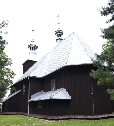 Zdjęcie nr 13: Kościół pw. św. Wawrzyńca w Grojcu jest drewnianą budowlą orientowaną, jednonawową z trójbocznie zamkniętym węższym prezbiterium od wschodu i wieżą od zachodu. Prostokątna nawa została wzniesiona na zrąb. Nawę i prezbiterium przykrywa dach siodłowy pokryty blachą cynkowaną. Do prezbiterium od północy przylega murowana zakrystia na rzucie prostokąta nakryta blaszanym dachem pulpitowym, a od południa prostokątny, drewniany aneks pełniący funkcję kaplicy bocznej, o podobnym dachu. Od północy do nawy dostawiono murowaną kaplicę na rzucie prostokąta przylegającą do zakrystii, a od południa niewielką czworoboczną kruchtę. Obie przestrzenie przykryto blaszanym dachem pulpitowym. W kruchcie południowej znajduje się drewniany portal z nadprożem w wykroju w ośli grzbiet. Nad wschodnią częścią nawy usytuowano sygnaturkę w kształcie wielobocznej latarni z krzyżem. Od zachodu do nawy dostawiono czworoboczną, drewnianą wieżę wzniesioną w konstrukcji słupowej, która w połowie nad nawą jest nadwieszona. Jej ściany są pionowe podzielone daszkami na trzy kondygnacje. Nakrywa ją blaszany, namiotowy hełm z latarnią zwieńczoną krzyżem. W przyziemiu wieży urządzono kruchtę. Wnętrze kościoła nakryto stropem z fasetą oddzieloną od ścian gzymsem. W zachodniej części nawy urządzono chór muzyczny zawieszony na dwóch kroksztynach i wsparty na kolumnach. W prezbiterium na ścianie wschodniej znajduje się ołtarz główny, a w nawie przy tęczy dwa ołtarze boczne oraz ambona.   