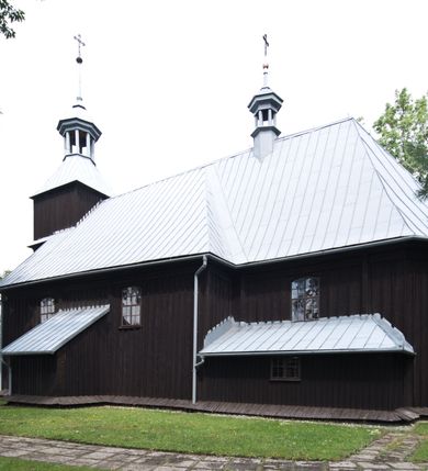 Zdjęcie nr 14: Kościół pw. św. Wawrzyńca w Grojcu jest drewnianą budowlą orientowaną, jednonawową z trójbocznie zamkniętym węższym prezbiterium od wschodu i wieżą od zachodu. Prostokątna nawa została wzniesiona na zrąb. Nawę i prezbiterium przykrywa dach siodłowy pokryty blachą cynkowaną. Do prezbiterium od północy przylega murowana zakrystia na rzucie prostokąta nakryta blaszanym dachem pulpitowym, a od południa prostokątny, drewniany aneks pełniący funkcję kaplicy bocznej, o podobnym dachu. Od północy do nawy dostawiono murowaną kaplicę na rzucie prostokąta przylegającą do zakrystii, a od południa niewielką czworoboczną kruchtę. Obie przestrzenie przykryto blaszanym dachem pulpitowym. W kruchcie południowej znajduje się drewniany portal z nadprożem w wykroju w ośli grzbiet. Nad wschodnią częścią nawy usytuowano sygnaturkę w kształcie wielobocznej latarni z krzyżem. Od zachodu do nawy dostawiono czworoboczną, drewnianą wieżę wzniesioną w konstrukcji słupowej, która w połowie nad nawą jest nadwieszona. Jej ściany są pionowe podzielone daszkami na trzy kondygnacje. Nakrywa ją blaszany, namiotowy hełm z latarnią zwieńczoną krzyżem. W przyziemiu wieży urządzono kruchtę. Wnętrze kościoła nakryto stropem z fasetą oddzieloną od ścian gzymsem. W zachodniej części nawy urządzono chór muzyczny zawieszony na dwóch kroksztynach i wsparty na kolumnach. W prezbiterium na ścianie wschodniej znajduje się ołtarz główny, a w nawie przy tęczy dwa ołtarze boczne oraz ambona.   