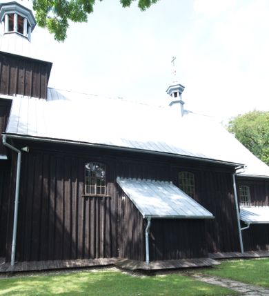 Zdjęcie nr 12: Kościół pw. św. Wawrzyńca w Grojcu jest drewnianą budowlą orientowaną, jednonawową z trójbocznie zamkniętym węższym prezbiterium od wschodu i wieżą od zachodu. Prostokątna nawa została wzniesiona na zrąb. Nawę i prezbiterium przykrywa dach siodłowy pokryty blachą cynkowaną. Do prezbiterium od północy przylega murowana zakrystia na rzucie prostokąta nakryta blaszanym dachem pulpitowym, a od południa prostokątny, drewniany aneks pełniący funkcję kaplicy bocznej, o podobnym dachu. Od północy do nawy dostawiono murowaną kaplicę na rzucie prostokąta przylegającą do zakrystii, a od południa niewielką czworoboczną kruchtę. Obie przestrzenie przykryto blaszanym dachem pulpitowym. W kruchcie południowej znajduje się drewniany portal z nadprożem w wykroju w ośli grzbiet. Nad wschodnią częścią nawy usytuowano sygnaturkę w kształcie wielobocznej latarni z krzyżem. Od zachodu do nawy dostawiono czworoboczną, drewnianą wieżę wzniesioną w konstrukcji słupowej, która w połowie nad nawą jest nadwieszona. Jej ściany są pionowe podzielone daszkami na trzy kondygnacje. Nakrywa ją blaszany, namiotowy hełm z latarnią zwieńczoną krzyżem. W przyziemiu wieży urządzono kruchtę. Wnętrze kościoła nakryto stropem z fasetą oddzieloną od ścian gzymsem. W zachodniej części nawy urządzono chór muzyczny zawieszony na dwóch kroksztynach i wsparty na kolumnach. W prezbiterium na ścianie wschodniej znajduje się ołtarz główny, a w nawie przy tęczy dwa ołtarze boczne oraz ambona.   