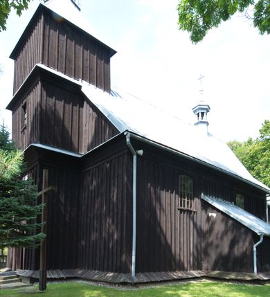 Zdjęcie nr 11: Kościół pw. św. Wawrzyńca w Grojcu jest drewnianą budowlą orientowaną, jednonawową z trójbocznie zamkniętym węższym prezbiterium od wschodu i wieżą od zachodu. Prostokątna nawa została wzniesiona na zrąb. Nawę i prezbiterium przykrywa dach siodłowy pokryty blachą cynkowaną. Do prezbiterium od północy przylega murowana zakrystia na rzucie prostokąta nakryta blaszanym dachem pulpitowym, a od południa prostokątny, drewniany aneks pełniący funkcję kaplicy bocznej, o podobnym dachu. Od północy do nawy dostawiono murowaną kaplicę na rzucie prostokąta przylegającą do zakrystii, a od południa niewielką czworoboczną kruchtę. Obie przestrzenie przykryto blaszanym dachem pulpitowym. W kruchcie południowej znajduje się drewniany portal z nadprożem w wykroju w ośli grzbiet. Nad wschodnią częścią nawy usytuowano sygnaturkę w kształcie wielobocznej latarni z krzyżem. Od zachodu do nawy dostawiono czworoboczną, drewnianą wieżę wzniesioną w konstrukcji słupowej, która w połowie nad nawą jest nadwieszona. Jej ściany są pionowe podzielone daszkami na trzy kondygnacje. Nakrywa ją blaszany, namiotowy hełm z latarnią zwieńczoną krzyżem. W przyziemiu wieży urządzono kruchtę. Wnętrze kościoła nakryto stropem z fasetą oddzieloną od ścian gzymsem. W zachodniej części nawy urządzono chór muzyczny zawieszony na dwóch kroksztynach i wsparty na kolumnach. W prezbiterium na ścianie wschodniej znajduje się ołtarz główny, a w nawie przy tęczy dwa ołtarze boczne oraz ambona.   