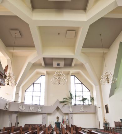 Zdjęcie nr 2: Orientowany kościół w Grojcu został wzniesiony jako świątynia salowa na rzucie wydłużonego prostokąta z nieznacznie wysuniętym poza zarys nawy transeptem. Nawę od wschodu kończy trójbocznie zamknięte prezbiterium, wpisane w obrys usytuowanej od wschodu prostokątnej zakrystii. Natomiast od zachodu zamyka ją nieznacznie wysunięta do przodu czworoboczna wieża, w przyziemiu której urządzono kruchtę. Wieżę wieńczy ostrosłupowy hełm z krzyżem wsparty na trójbocznych przyczółkach zamykających u góry płaszczyzny ścian bocznych. Poniżej hełmu widocznie są trójkątnie zamknięte, prostokątne okna, a pod nimi na ścianie zachodniej zainstalowany zegar. Po bokach wieży ściany nawy zostały przeprute monumentalnymi, trapezoidalnymi oknami doświetlającymi chór muzyczny i wnętrze świątyni. Podobne okna wprowadzono w ścianie południowej i północnej transeptu. Wnętrze kościoła nakryto żelbetonowym, płaskim stropem wspartym na łamanych filarach, stanowiących stylizowaną wersję sklepienia lustrzanego. W części zachodniej nawy oraz w ramionach transeptu wprowadzono połączone ze sobą empory. Na emporze zachodniej urządzono chór muzyczny ze współczesnym prospektem organowym. Prezbiterium zostało podniesione o kilka stopni w stosunku do poziomu posadzki nawy.  Ustawiono w nim marmurowy ołtarz posoborowy oraz ambonkę, dekorując środkową ścianę prezbiterium monumentalną, rzeźbioną postacią Chrystusa Zmartwychwstałego. Na ścianie północnej zawieszono w dekoracyjnej, romboidalnej ramie wizerunek Matki Boskiej Ostrobramskiej. 