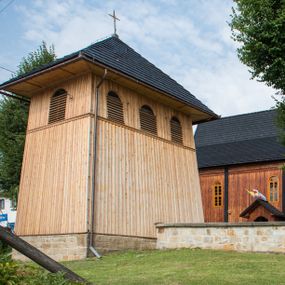 Zdjęcie nr 1: Dzwonnica drewniana, konstrukcji słupowej, ściany szalowane z listowaniem, więźba dachowa drewniana. Założona na planie prostokąta, na kamiennym podmurowaniu. Ściany zwężające się ku górze, odcięte listwami w trzech czwartych wysokości. Dach gontowy, czterospadowy, zakończony krzyżem. Otwór drzwiowy w ścianie południowej o wykroju stojącego prostokąta zamknięty drzwiami szalowanymi z listowaniem. Ponad nimi, na osi otwór w formie stojącego prostokąta zamkniętego łukiem odcinkowym, zamknięty drzwiczkami szalowanymi z listowaniem. Otwór nakryty gontowym daszkiem okapowym. W najwyższej partii ścian otwory głosowe w formie stojącego prostokąta zamkniętego łukiem półkolistym nadwieszonym po trzy na wschodniej i zachodniej ścianie i jednym na północnej. 